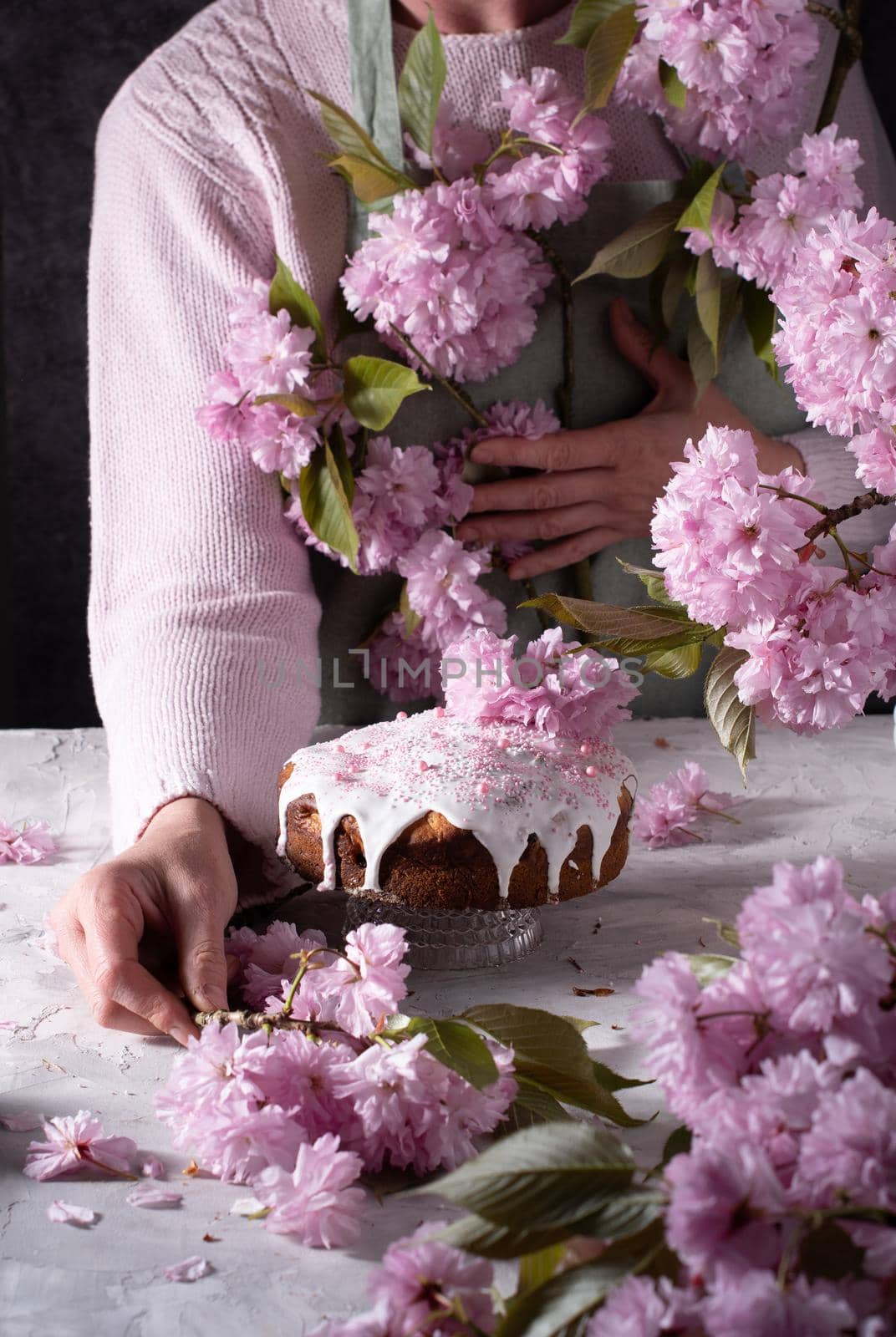 a woman decorates a homemade Easter cake with pink sakura flowers,spring blossom by KaterinaDalemans