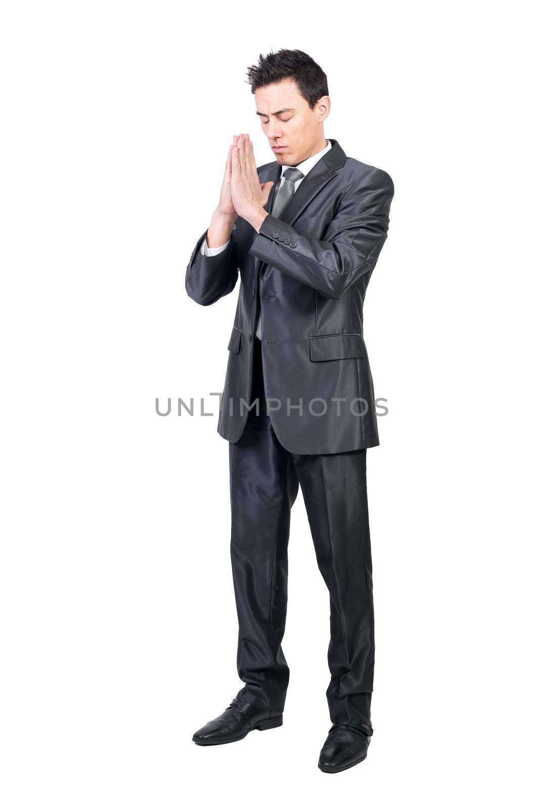 Full body of hoping peaceful male worker in classy suit standing with prayer hands in studio against white background