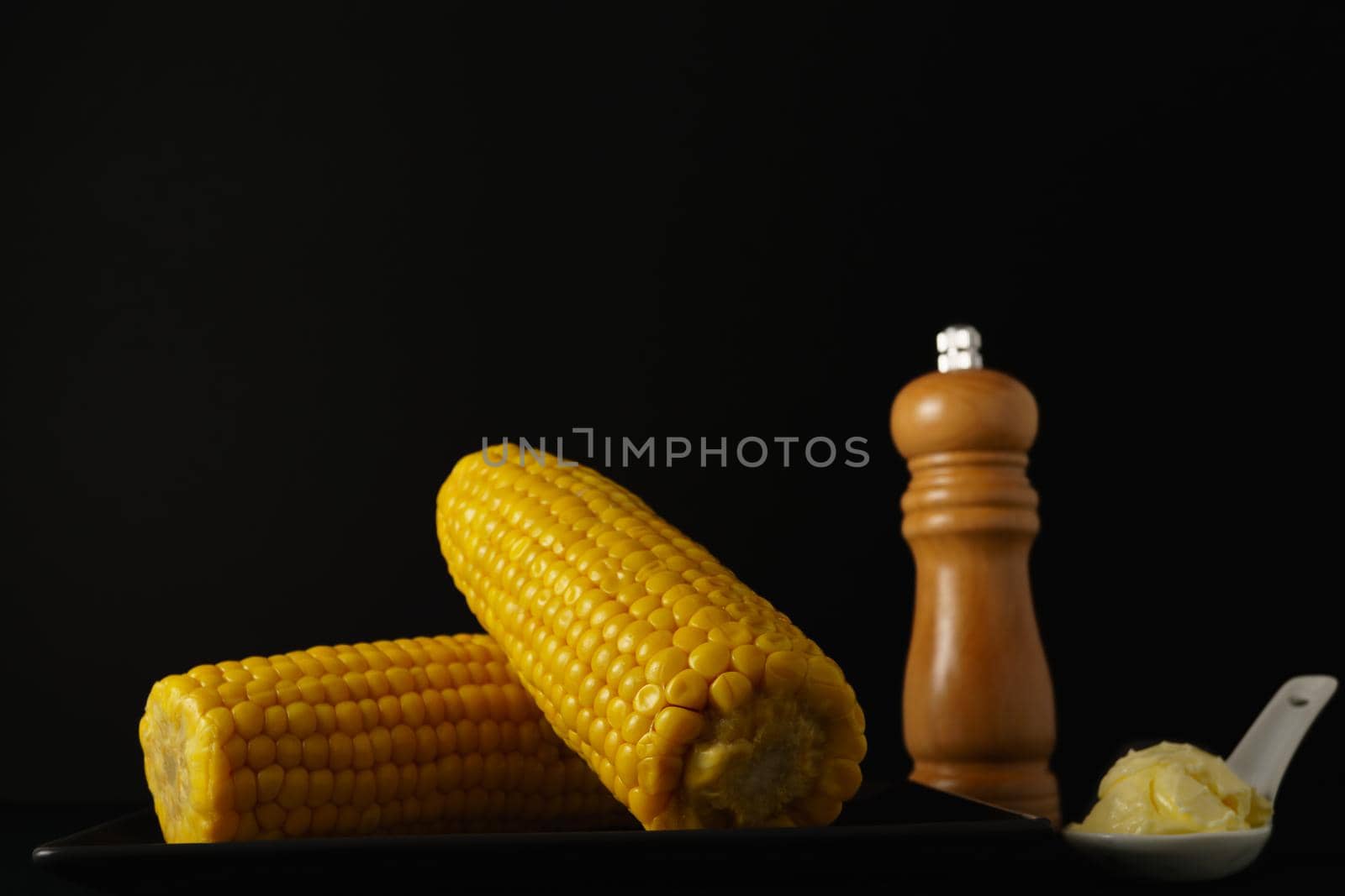 corn on the cob with pepper and butter in a white ceramic spoon isolated on black background