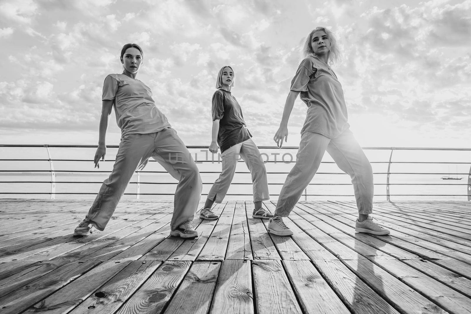Dancing group of young talented freak women performing freestyle hip-hop moves. females enjoying modern dance expression. Outdoor training near sea or ocean during sunset. High quality photo