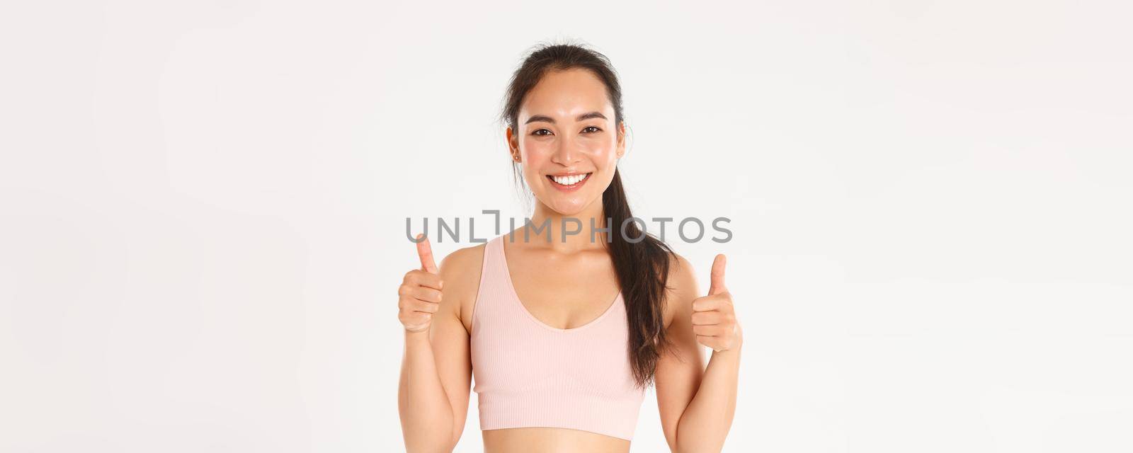 Sport, wellbeing and active lifestyle concept. Close-up of happy cute brunette asian girl, fitness instructor looking satisfied, showing thumbs-up and smiling in approval, praise good workout.