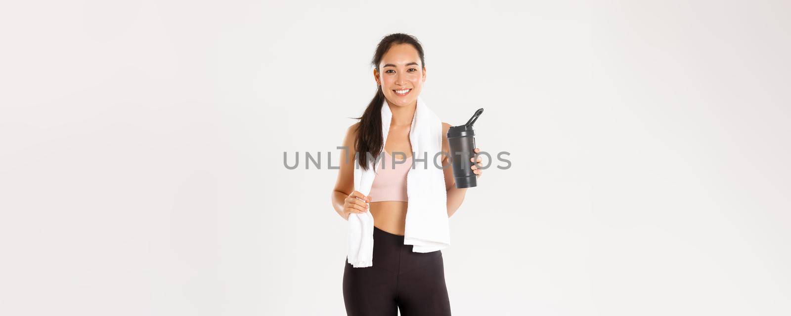 Sport, wellbeing and active lifestyle concept. Portrait of satisfied attractive asian fitness girl with cute smile, looking pleased wiping sweat with towel and drinking water after workout by Benzoix