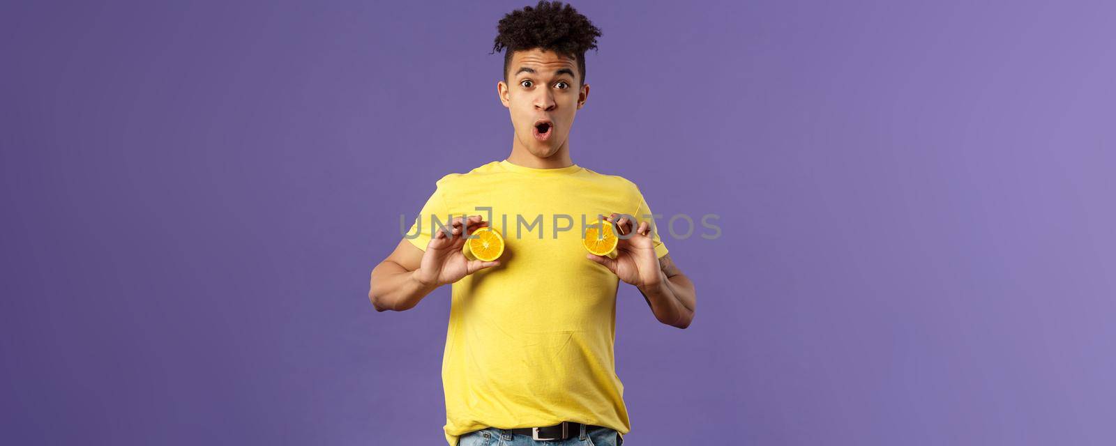 Holidays, vitamins and vacation concept. Portrait of funny and cute young 25s man fool around, showing breast with pieces of oranges over chest, look ashamed or shocked, purple background by Benzoix