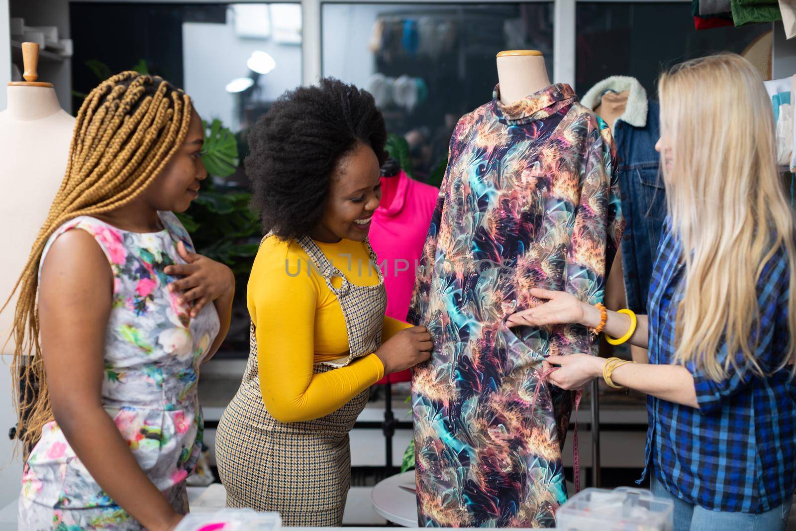 A clothing designer shows a dress from her new collection to two interested clients. Two African women and a European woman in the tailor's workshop.