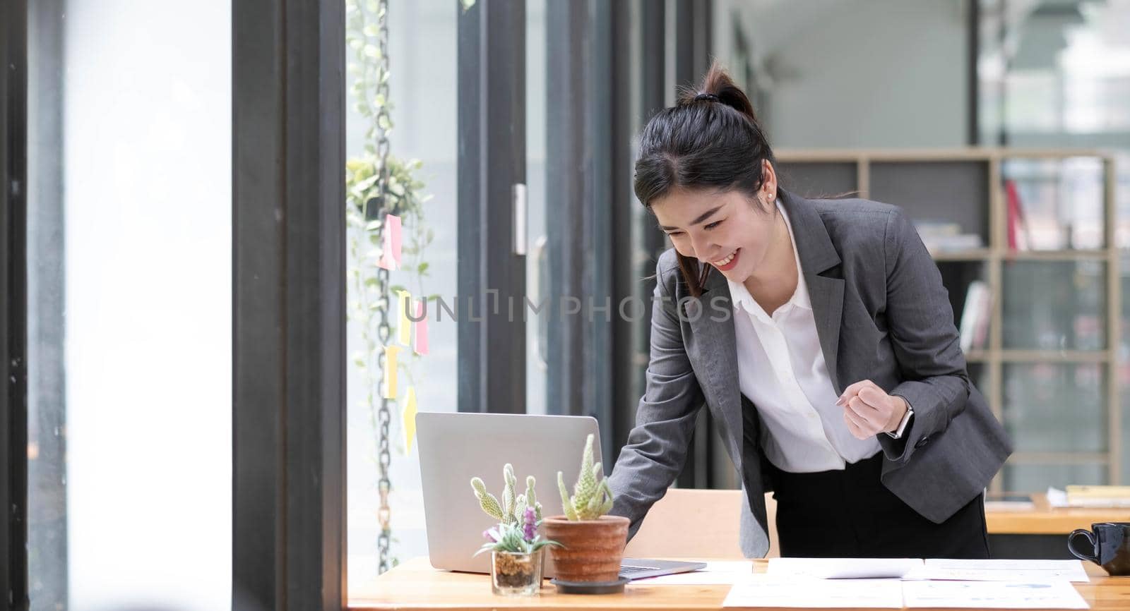 Happy excited successful Asian businesswoman triumphing with a laptop computer smartphone in the workplace office.