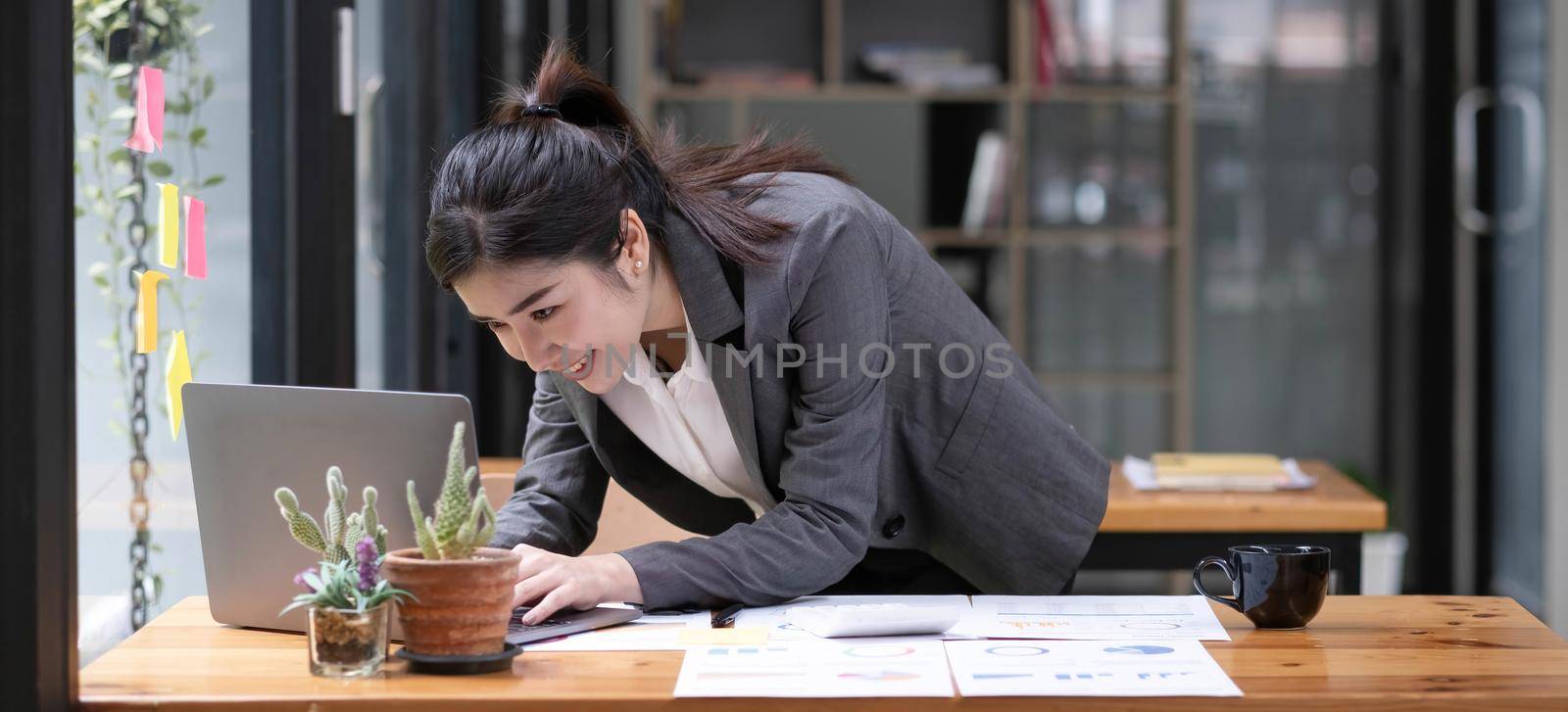 Happy attractive Asian business woman working with a laptop and financial document at office, successful action, Business concept..