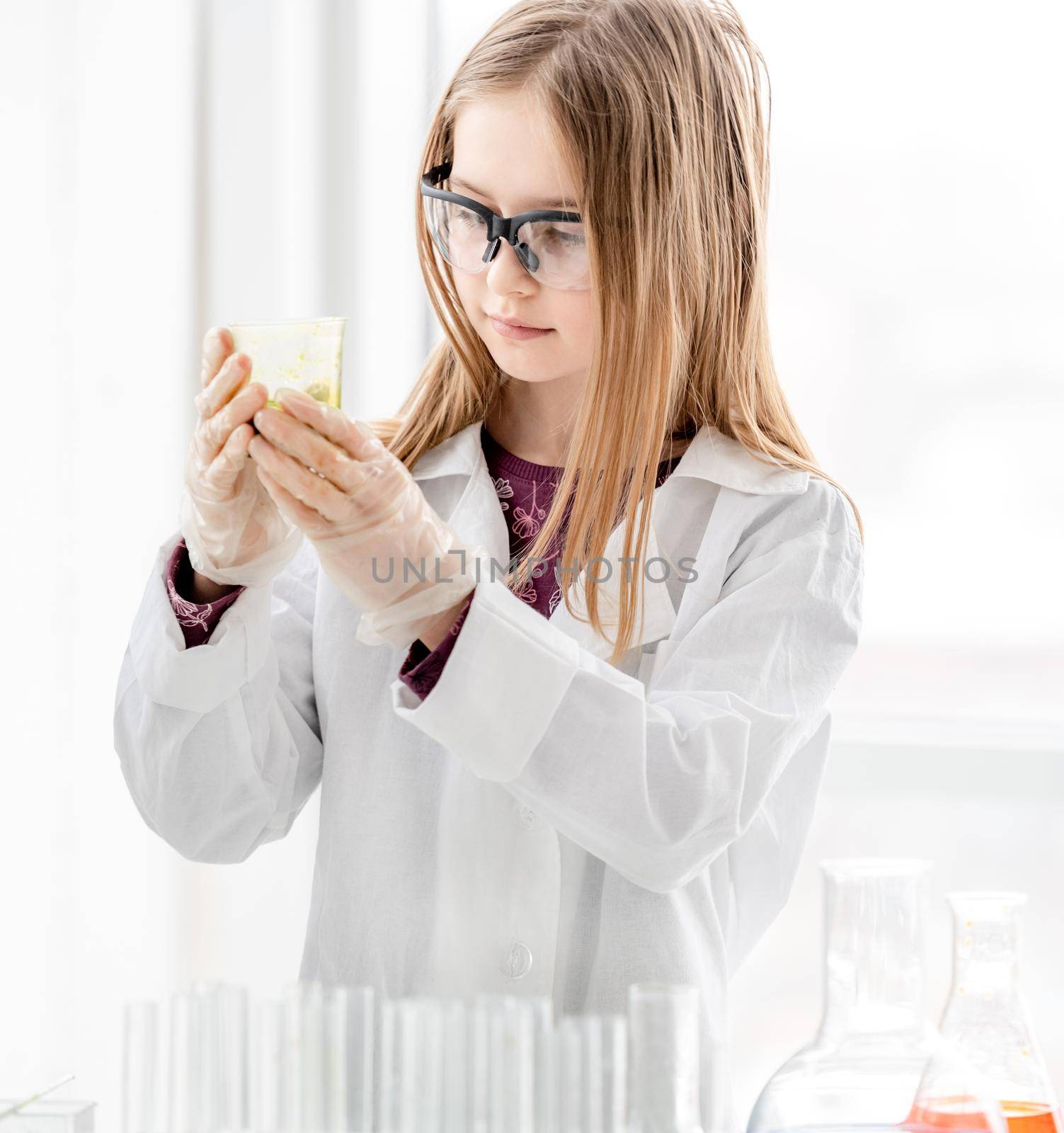 Smart girl during scientific chemistry experiment wearing protection glasses, holding tubes and measuring ingridients. Schoolgirl with chemical equipment on school lesson