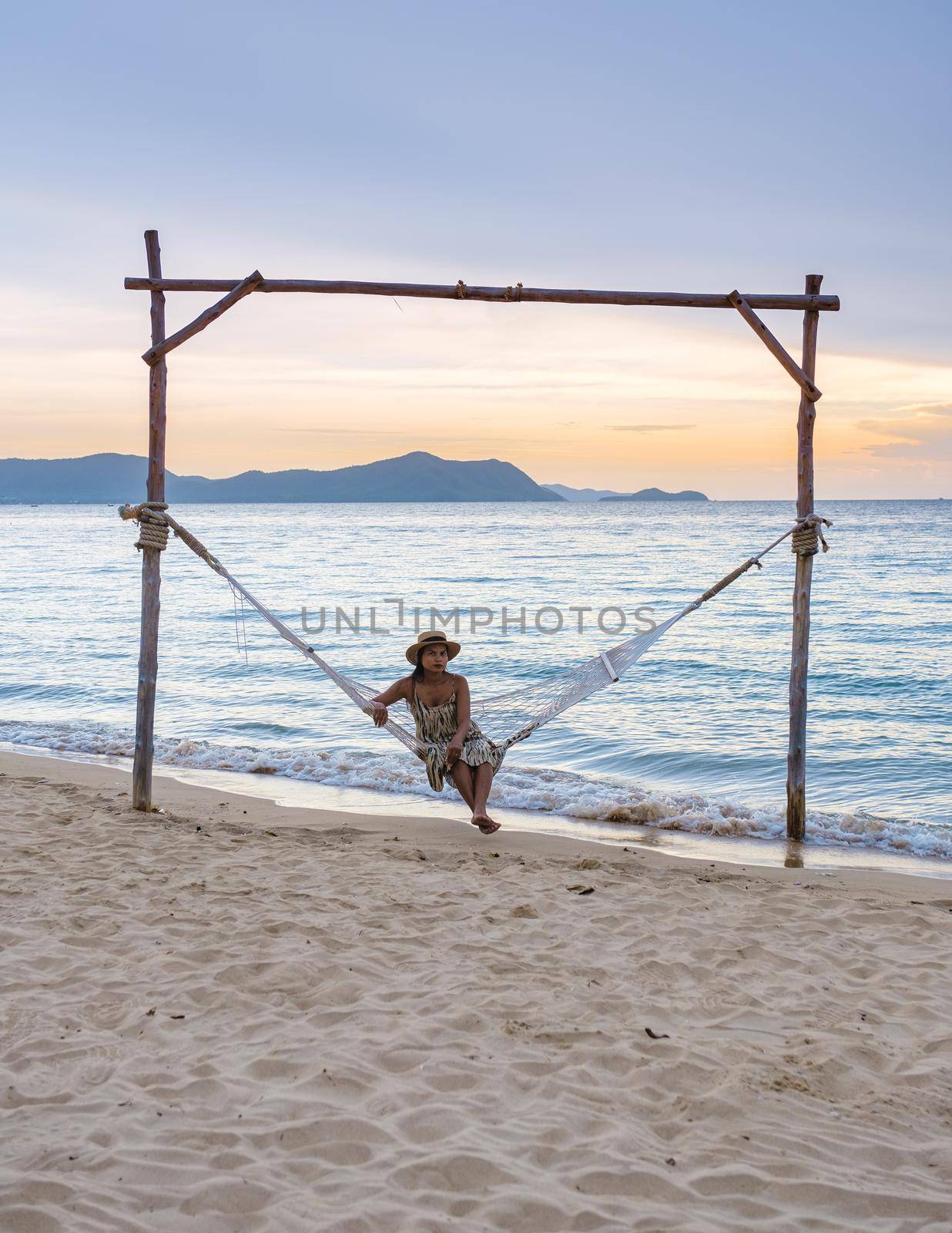 Men and women watching the sunset in a hammock on the Pattaya beach during sunset in Thailand Ban Amphur beach. couple walking on a tropical beach with palm tree and hammock during sunset