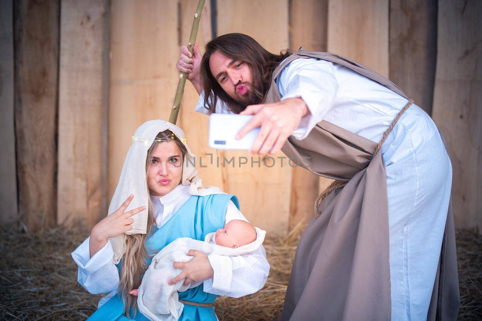 Biblical characters of the virgin mary and joseph taking a selfie while joking in a crib