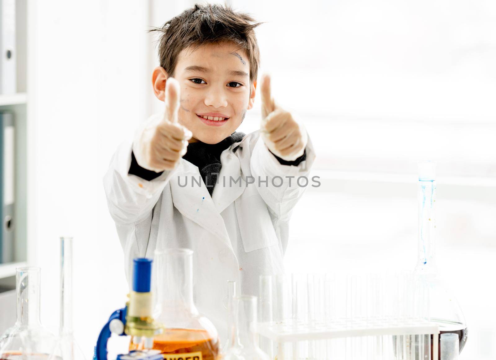 School boy showing super with hands holding big fingers up during chemistry experiment in elementary science class. Clever pupil kid in lab