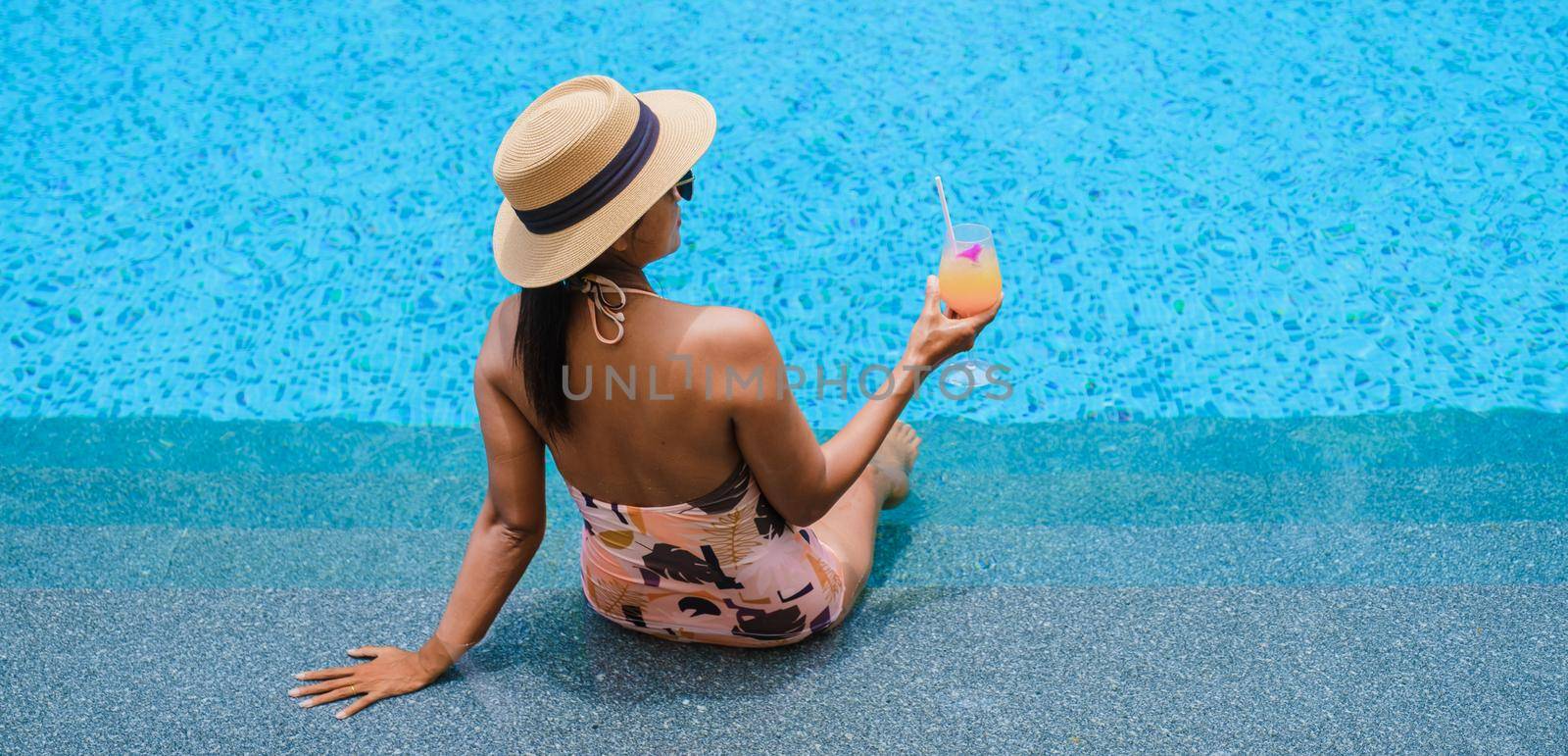 Asian women with a hat relaxing in the swimming pool with a cocktail in hand, women swimming pool banner holiday vacation concept, Asian women in blue swimming pool luxury vacation