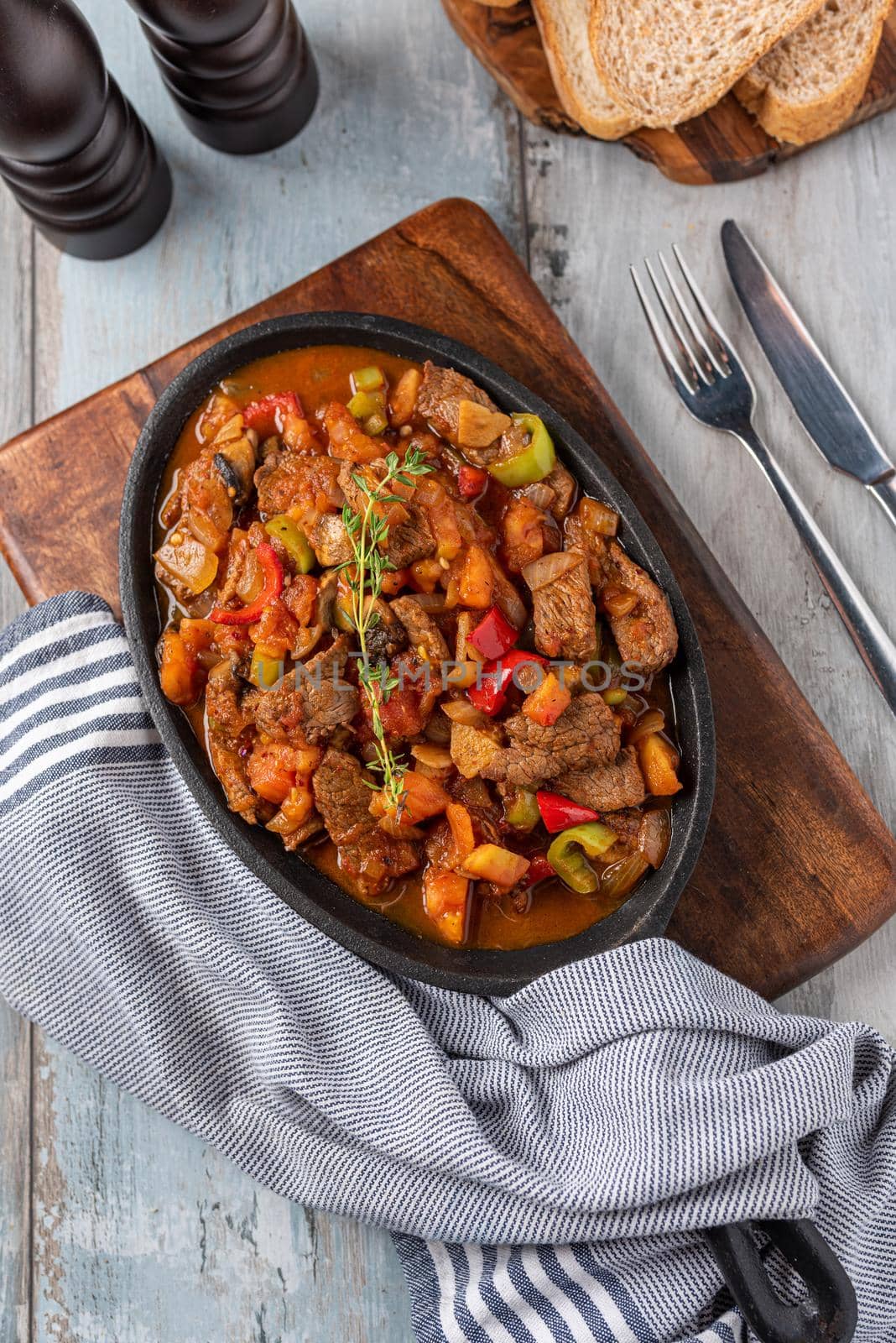 Beef stew with potatoes, carrots and herbs in iron casserole, top view