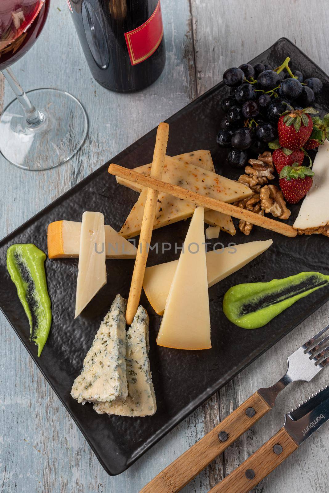 Cheese plate served with grapes, strawberry, crackers and nuts on a wooden background