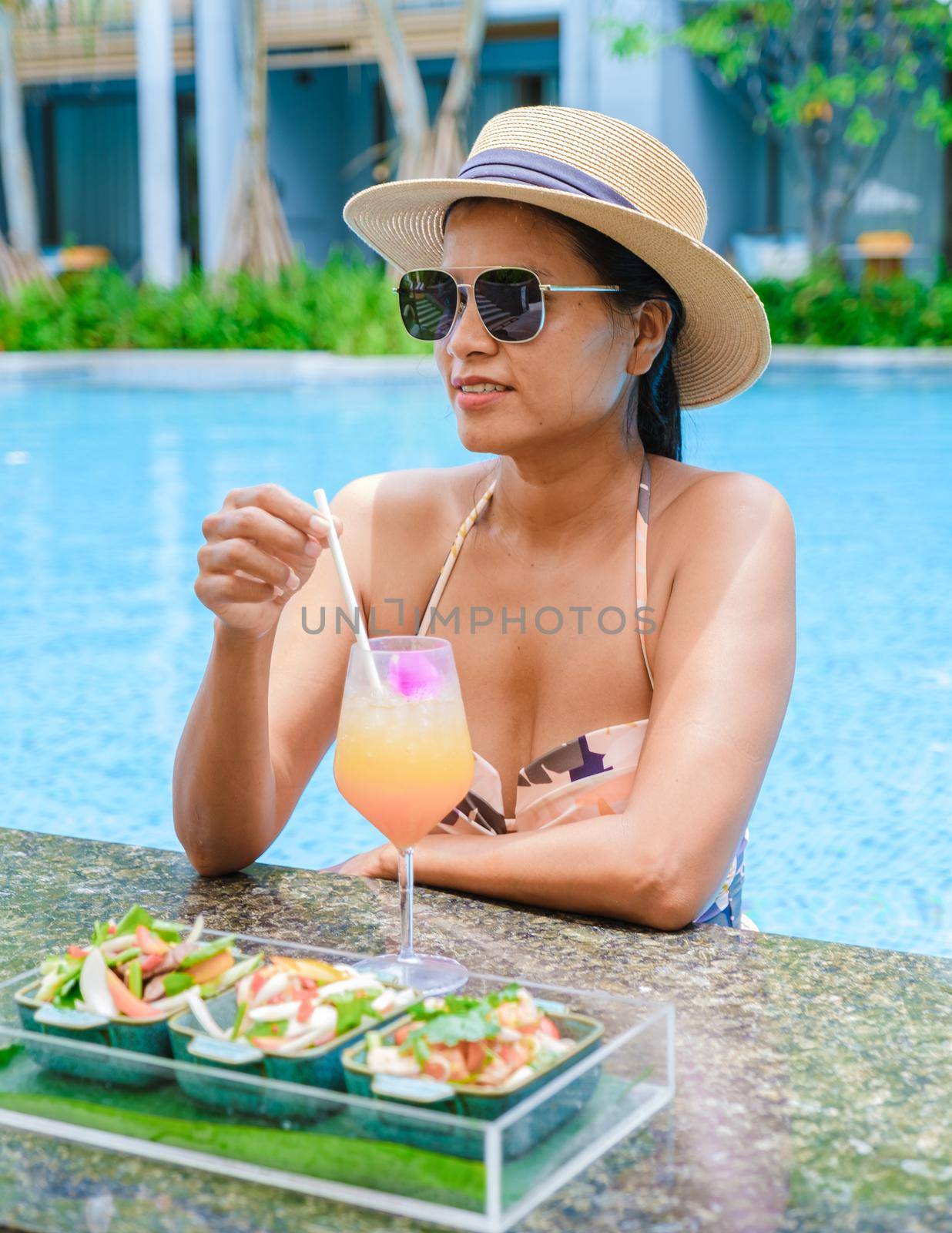 Asian women with a hat relaxing in the swimming pool with a cocktail in hand, women swimming pool banner holiday vacation concept, Asian women in blue swimming pool luxury vacation