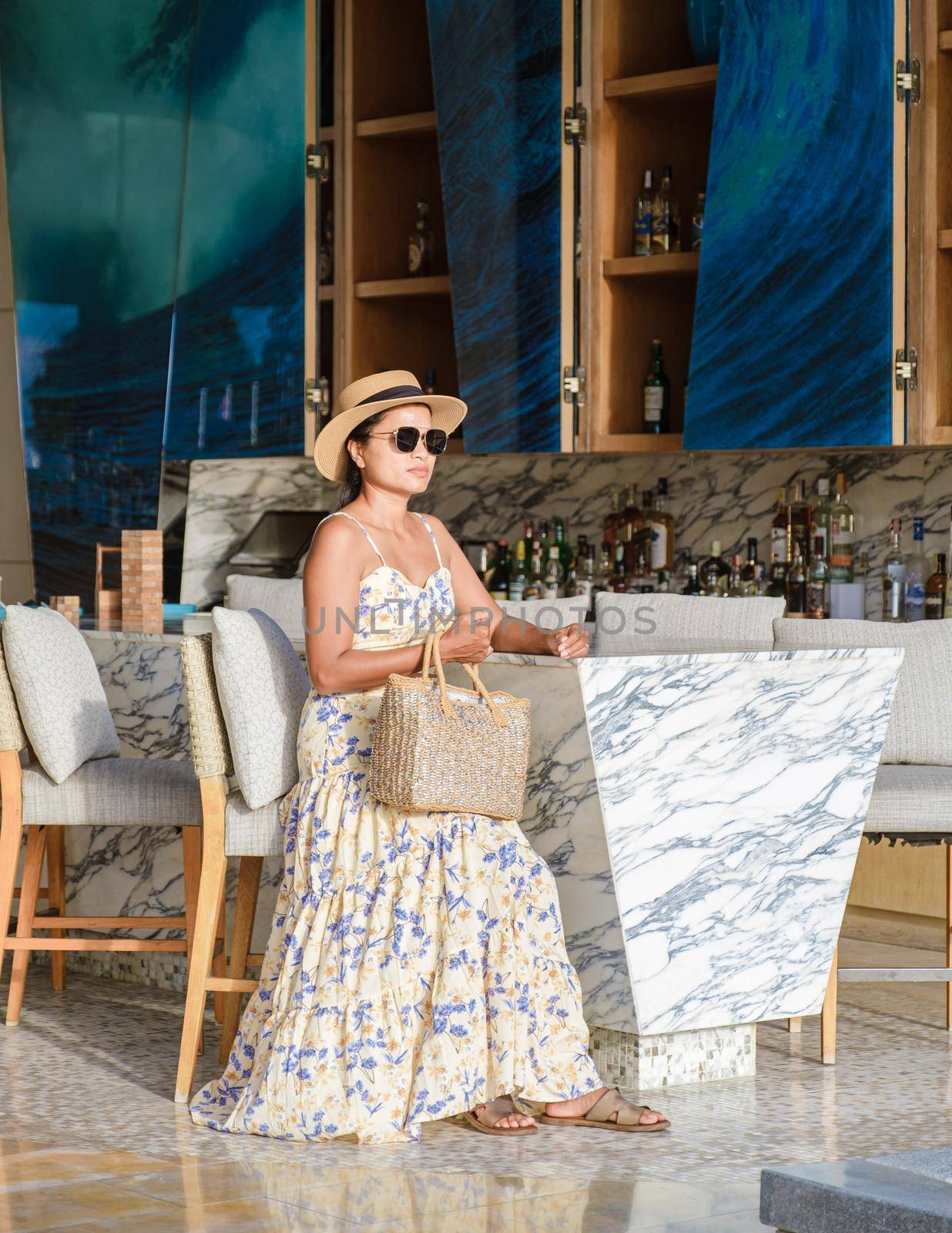 Asian women with a hat relaxing at the bar in a hotel during a luxury vacation. women by the bar during sunset