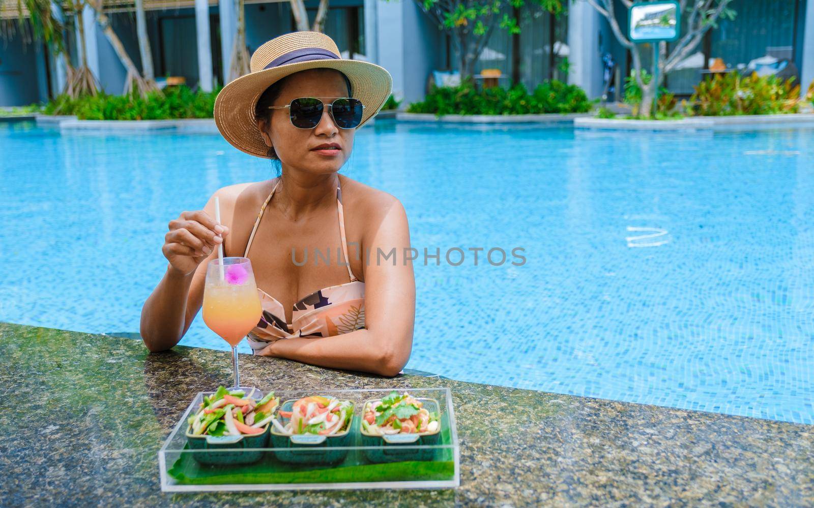 Asian women with a hat relaxing in the swimming pool with a cocktail in hand, women swimming pool banner holiday vacation concept, Asian women in blue swimming pool luxury vacation