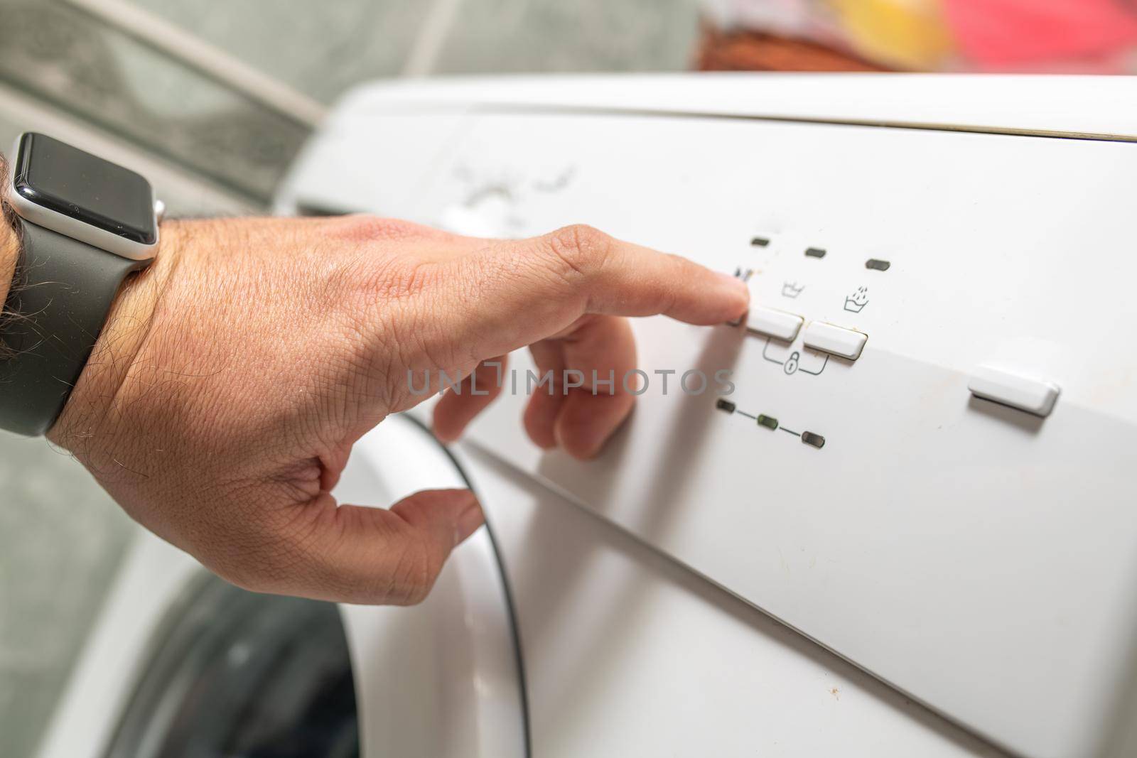 Male hand pressing washing machine buttons before doing the laundry