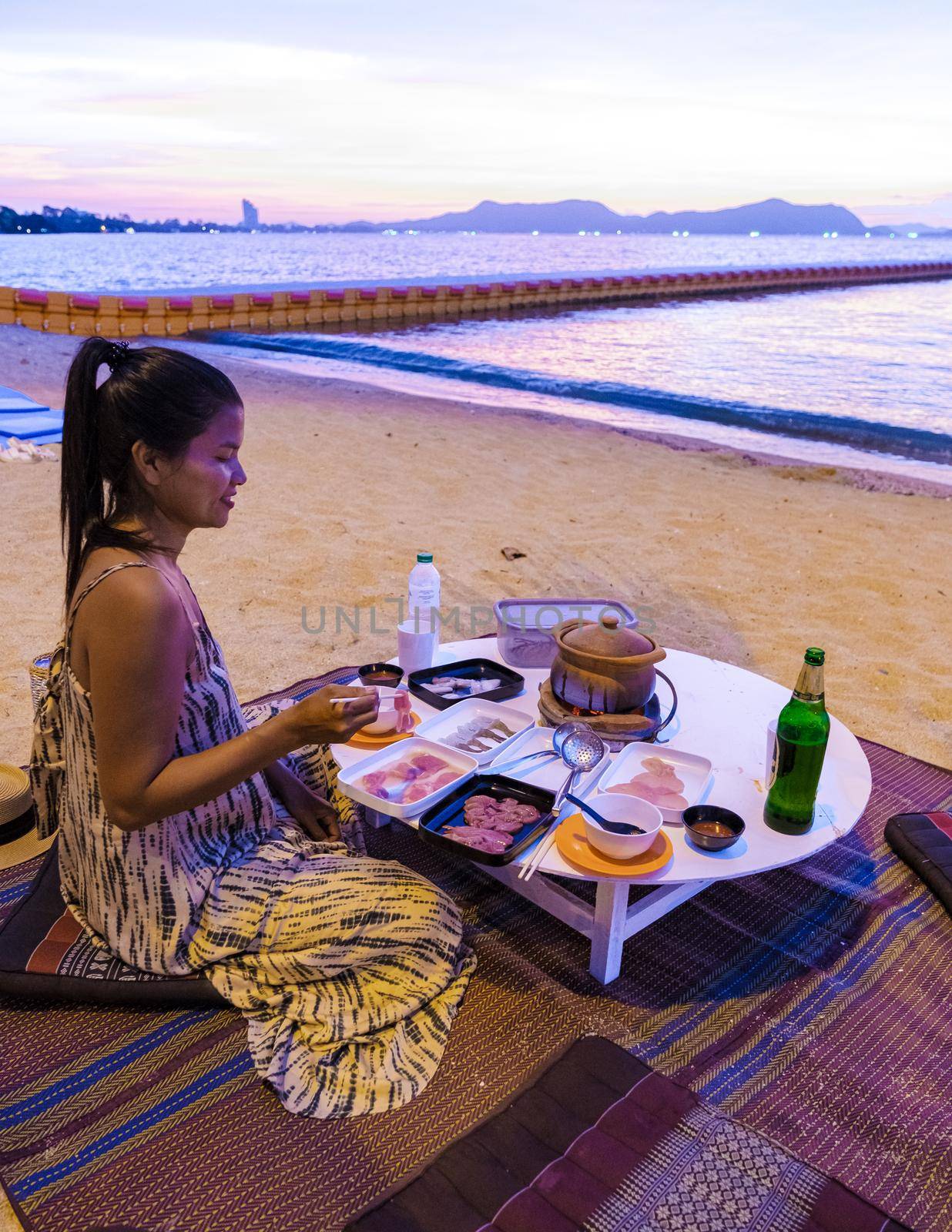 women bbq cooking noodle soup during sunset in Thailand Ban Amphur beach. relaxing with bbq Thai traditional on a tropical beach with palm trees and hammock during sunset