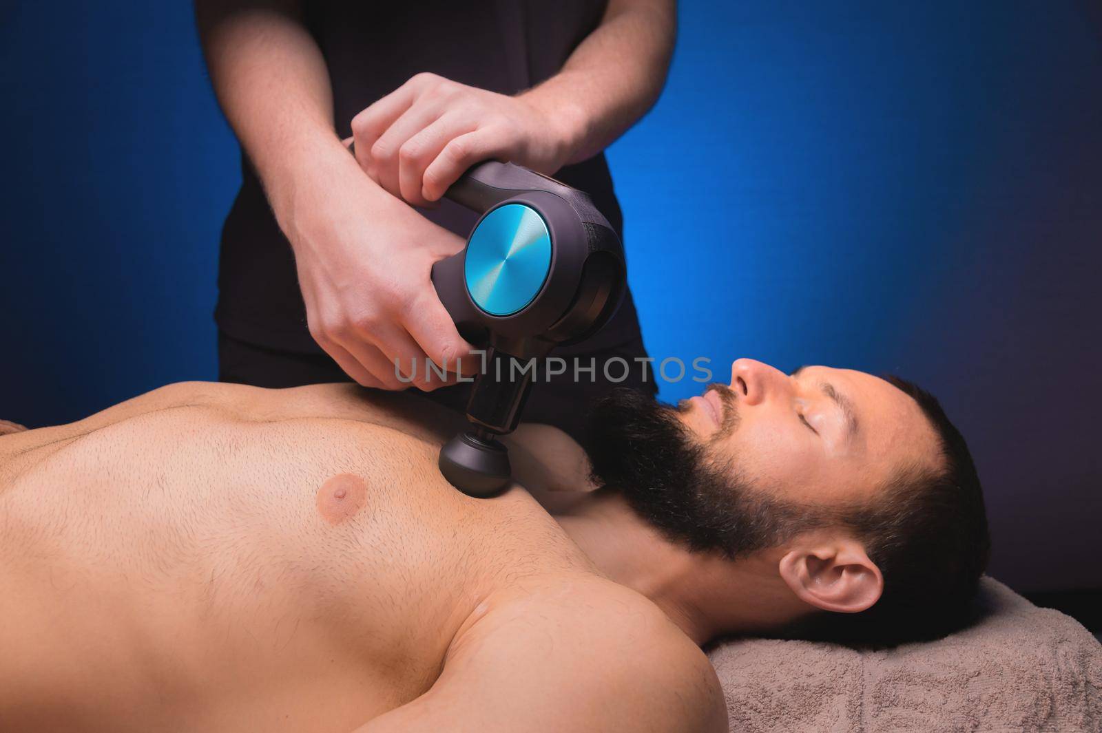 Sports percussion massage in the medical office of the gym. The masseur makes massage exercises. Percussion therapy for regenerating sports body massage. Sports injury rehabilitation concepts
