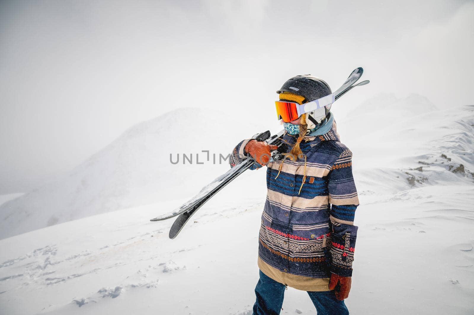 Portrait of a pretty and active woman skier, wearing a mask and holding skis in her hands, active winter holidays by yanik88