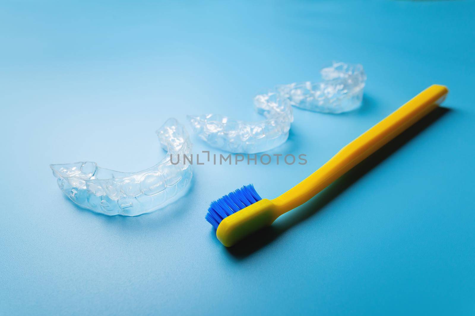 An invisible plastic aligner for correcting teeth to straighten teeth lies on a blue background with a toothbrush.