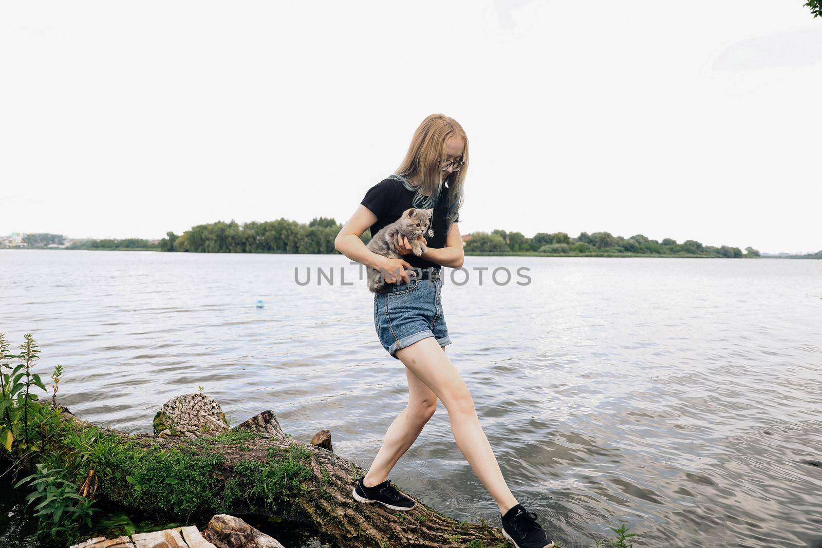 A young woman walks with a three month old Scottish Reed kitten near the lake in summer. The photo was taken in the general plan in sunny weather with natural light