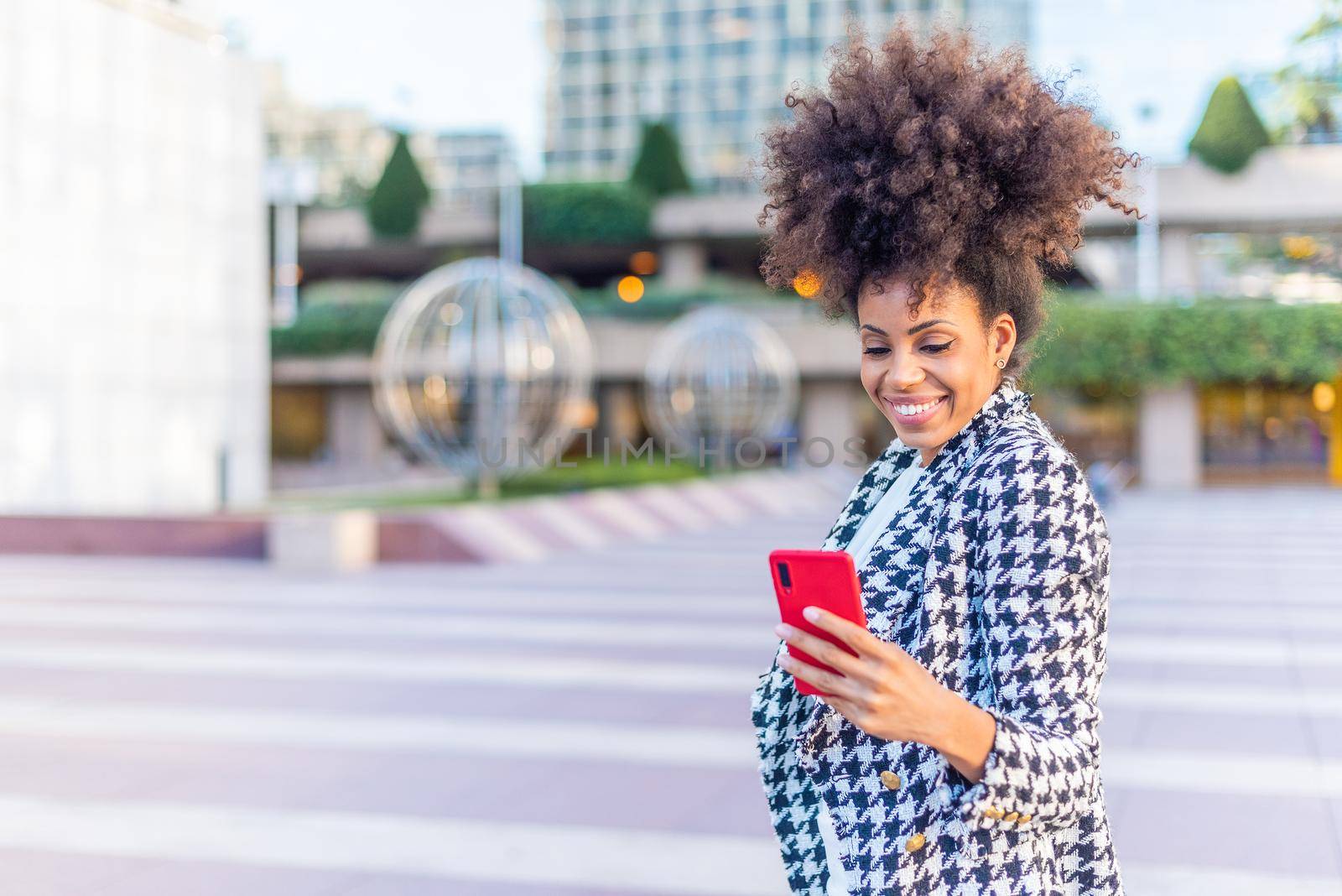 black afro woman looking happily to the phone while standing in the street