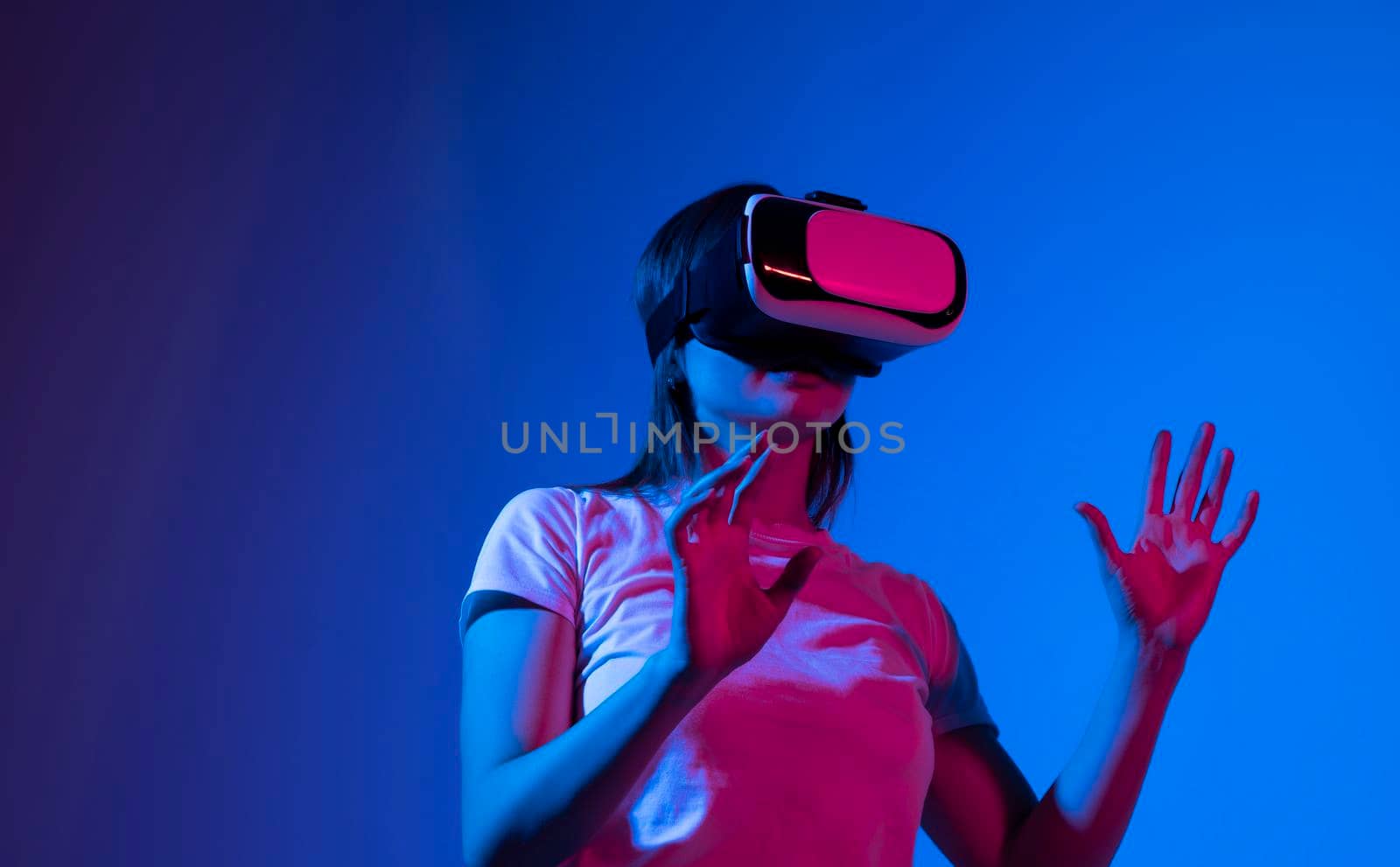 Young woman wearing VR headset while working with engineering project in lab with three dimensional printing in neon light studio. High tech engineering concept