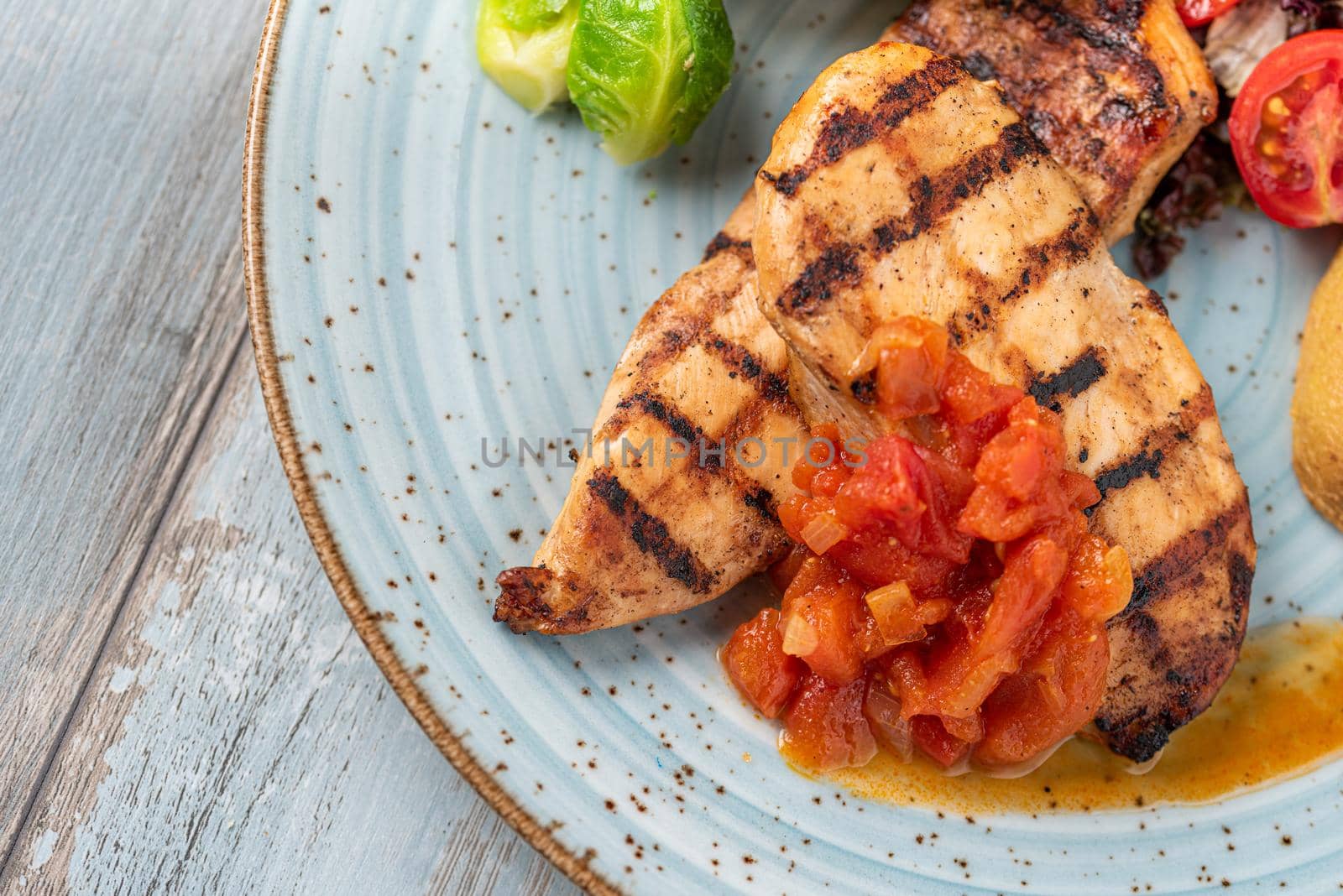 Grilled chicken breast in different variations with cherry tomatoes and different vegetables on wooden background