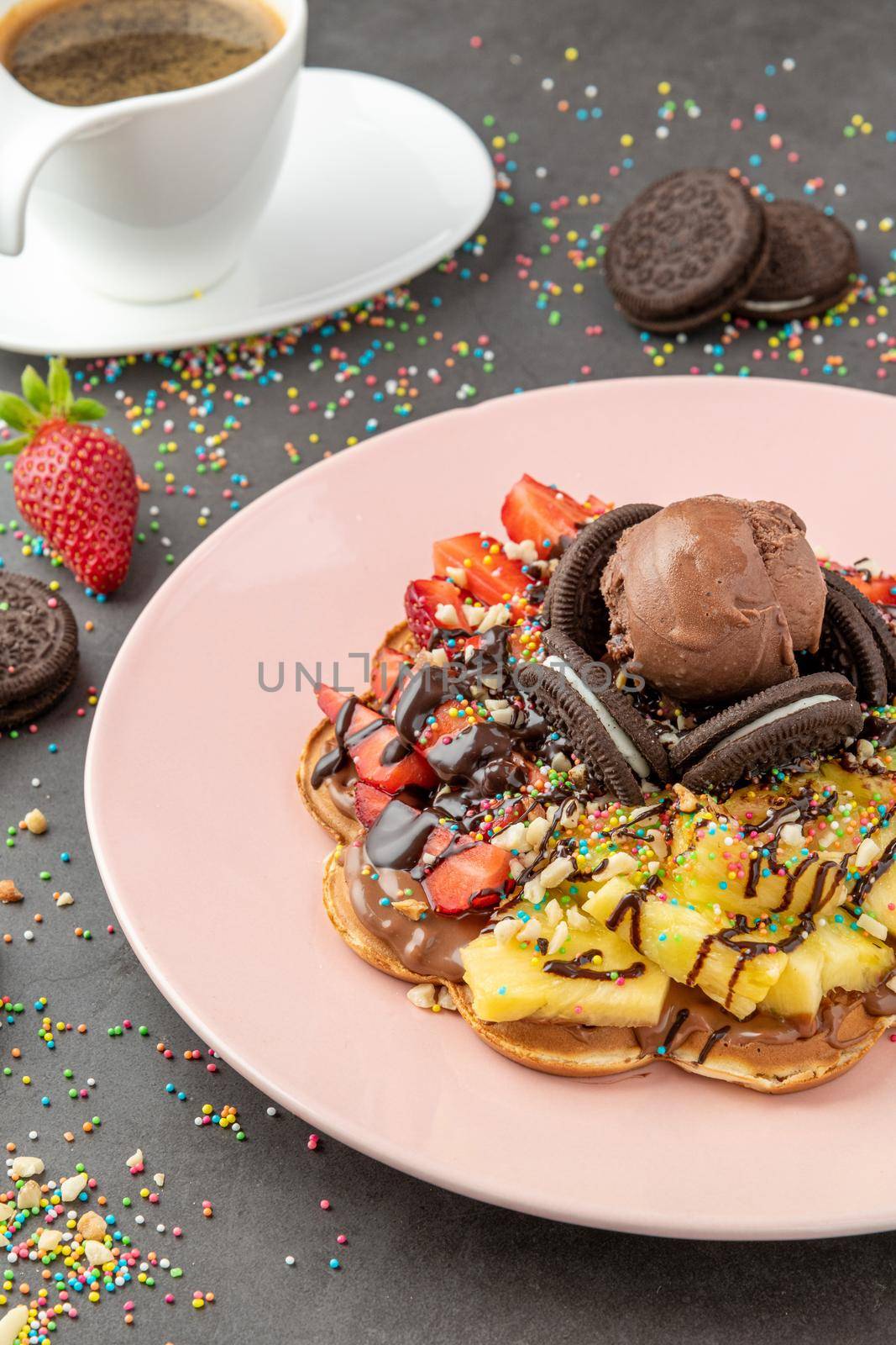 Heart waffle with pineapple and strawberry with gummy candy and ice cream on it.