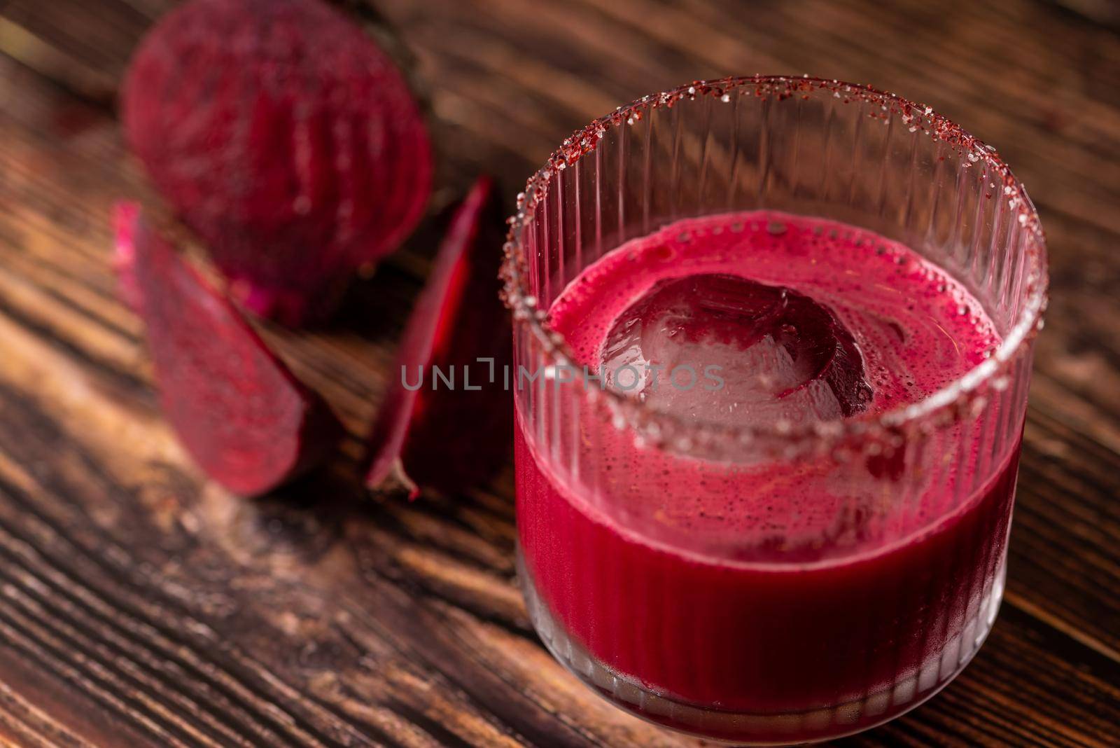 Alcoholic beetroot cocktail beverage in elegant glass on wooden table.