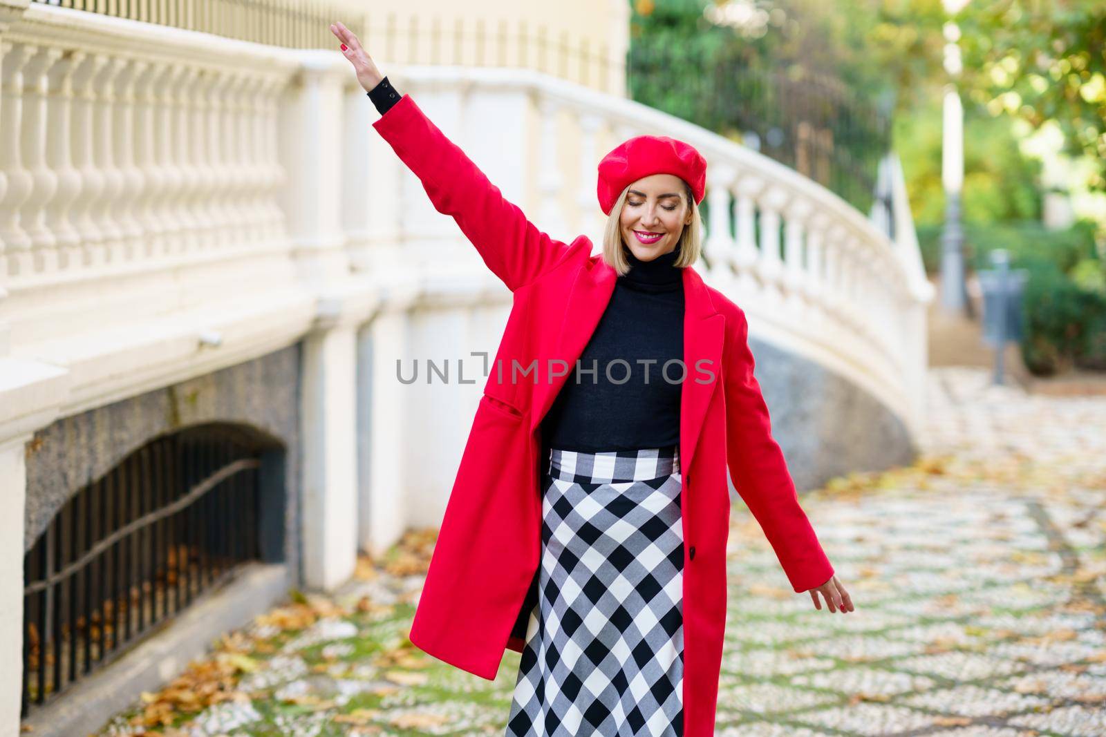 Cheerful woman in stylish wear walking near fence by javiindy