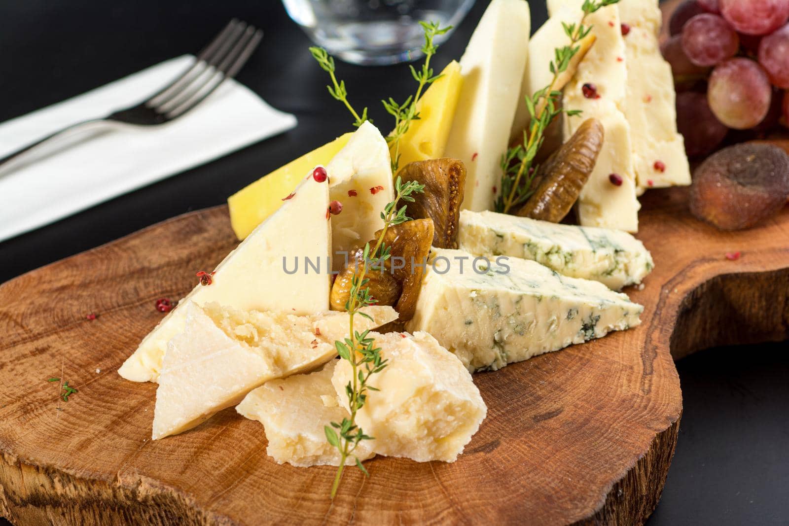Cheese plate served with grapes, jam, figs, crackers and walnuts on a dark stone background