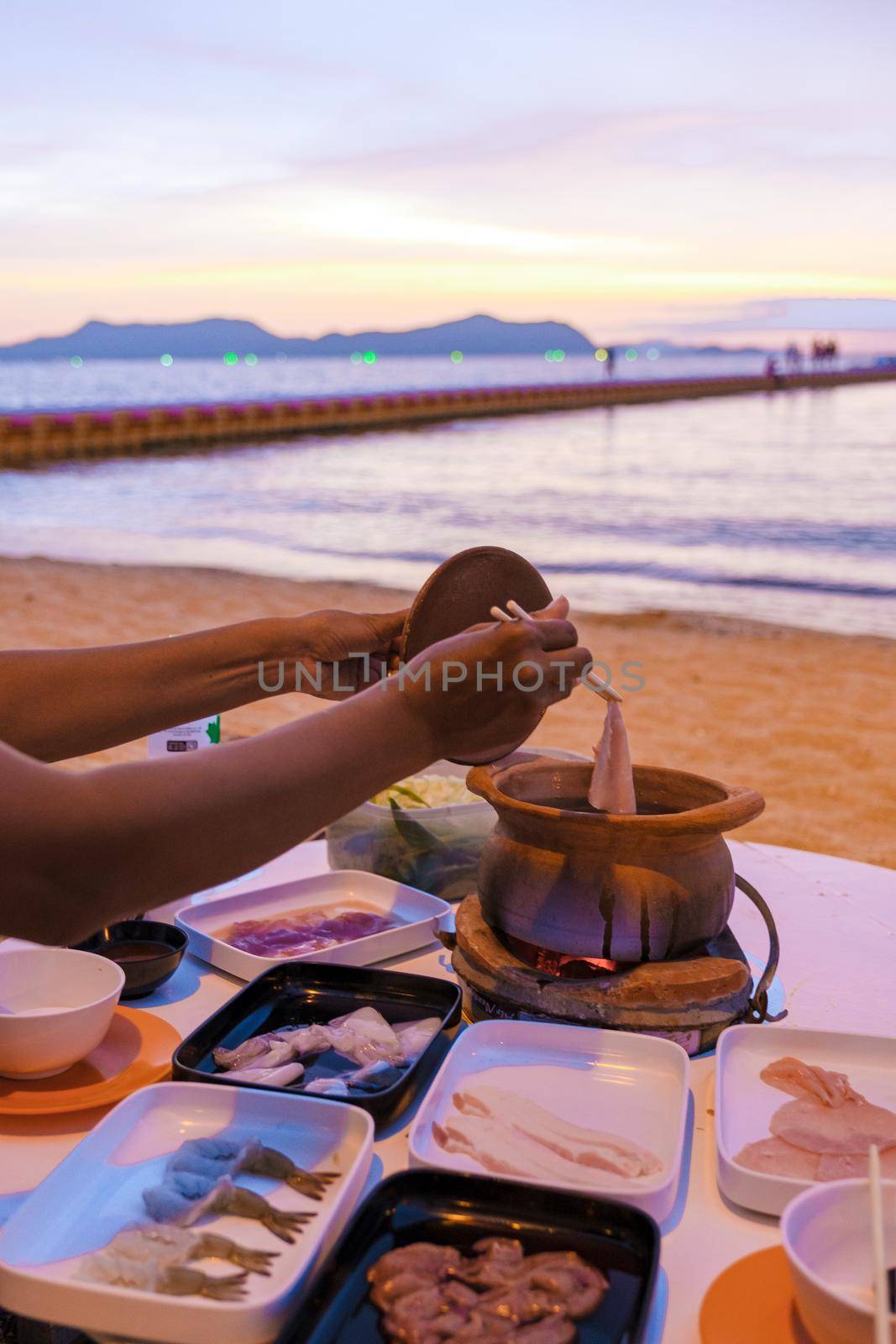 women bbq cooking noodle soup during sunset in Thailand Ban Amphur beach. relaxing with bbq Thai traditional on a tropical beach with palm trees and hammock during sunset