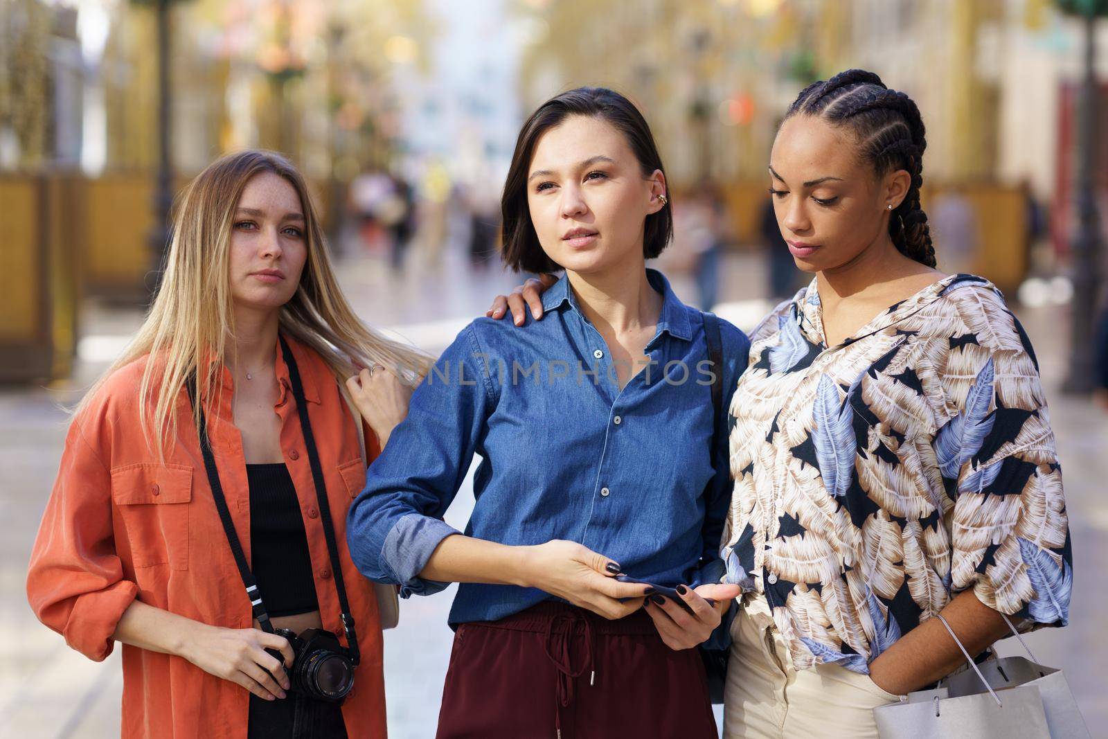 Stylish young multiracial female best friends on casual outfits standing together on city street during vacation on sunny day