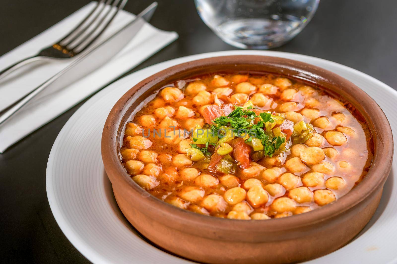 Traditional chickpeas dish in casserole on black stone table.