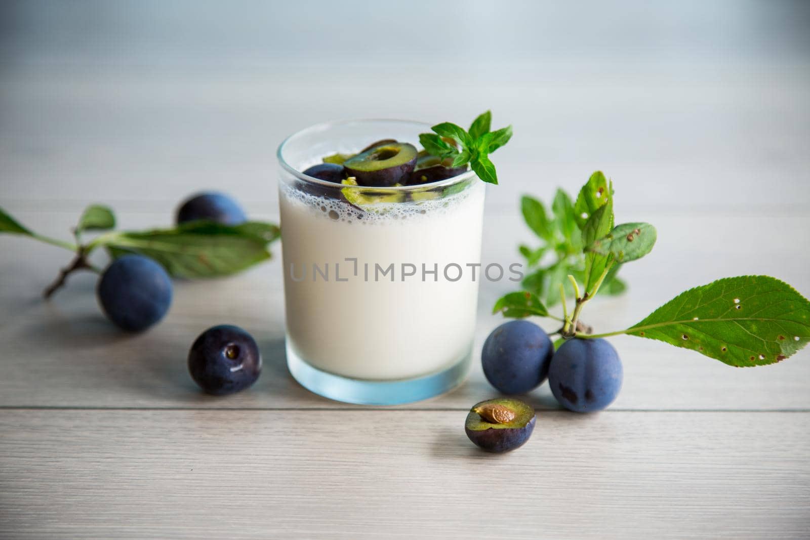 sweet homemade yogurt with fresh plum slices in a glass on a wooden table