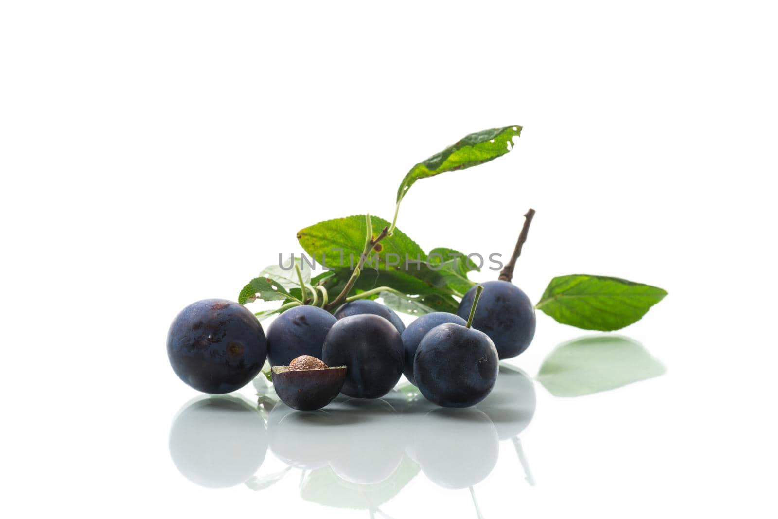 Ripe whole round plums with leaves isolated on white background.