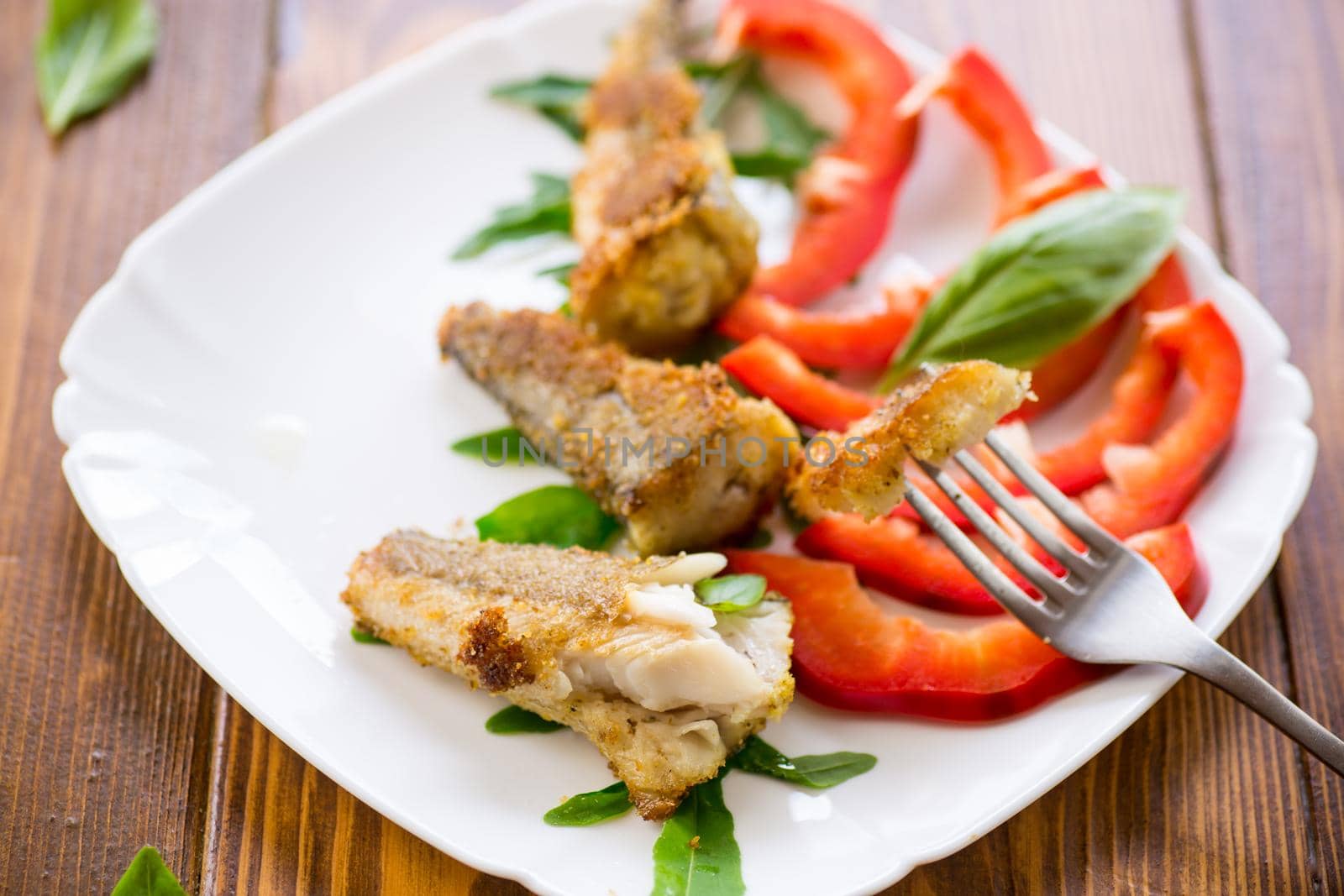 Pieces of fried hake fish in a plate with pepper on a wooden table
