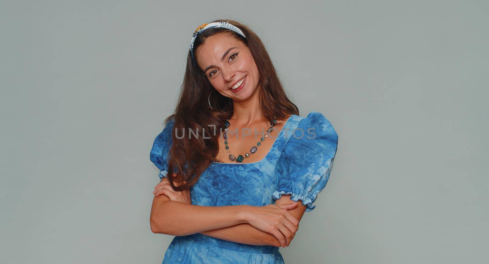 Portrait of happy lovely pretty young woman in blue princess dress looking at camera, smiling. Adult stylish female girl isolated alone on gray studio wall background indoors. Female nature beauty