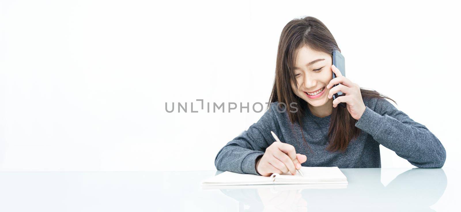 Close up woman long hair writing notebook and using mobile phone on white background