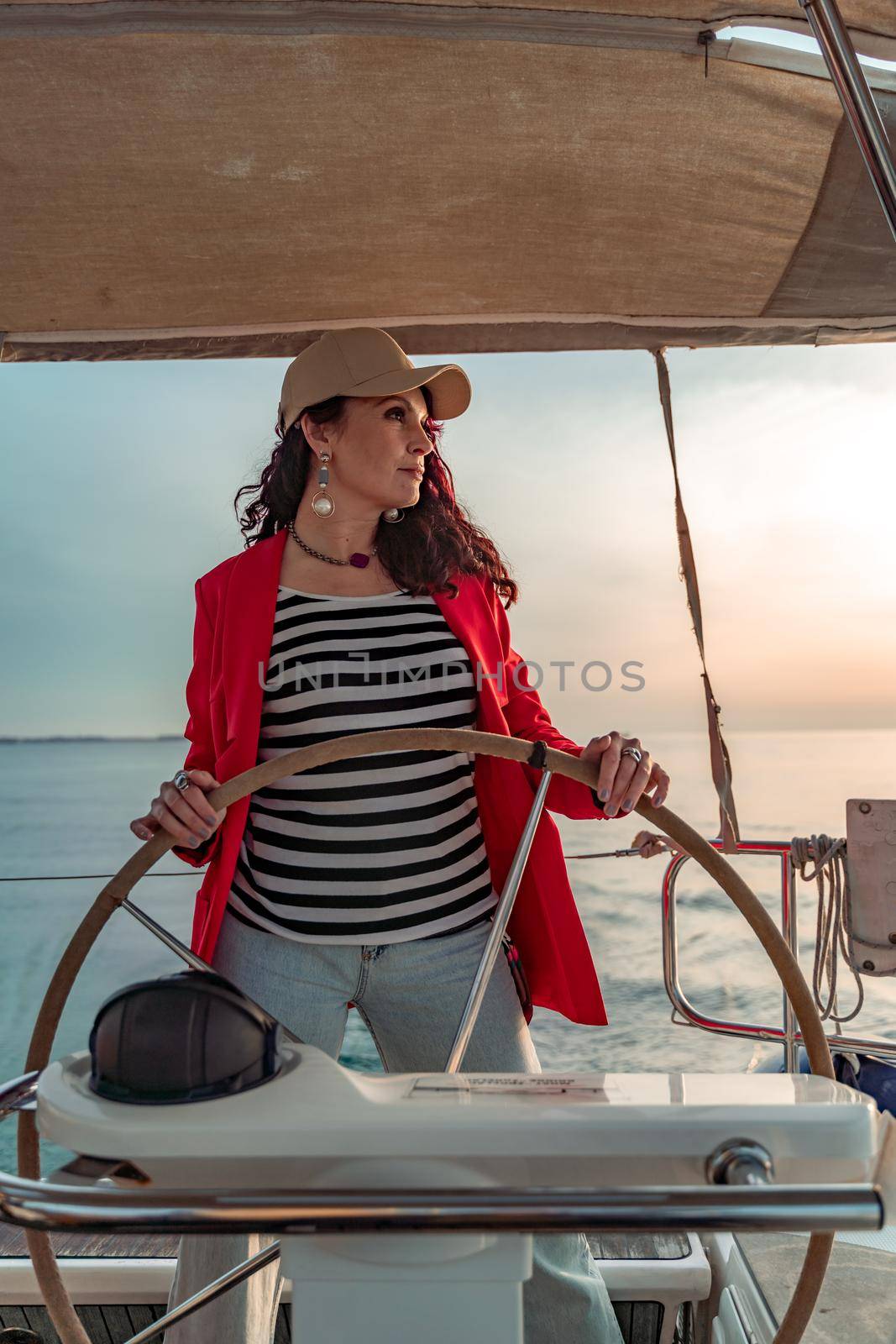 Attractive middle-aged woman at the helm of a yacht on a summer day. Luxury summer adventure, outdoor activities