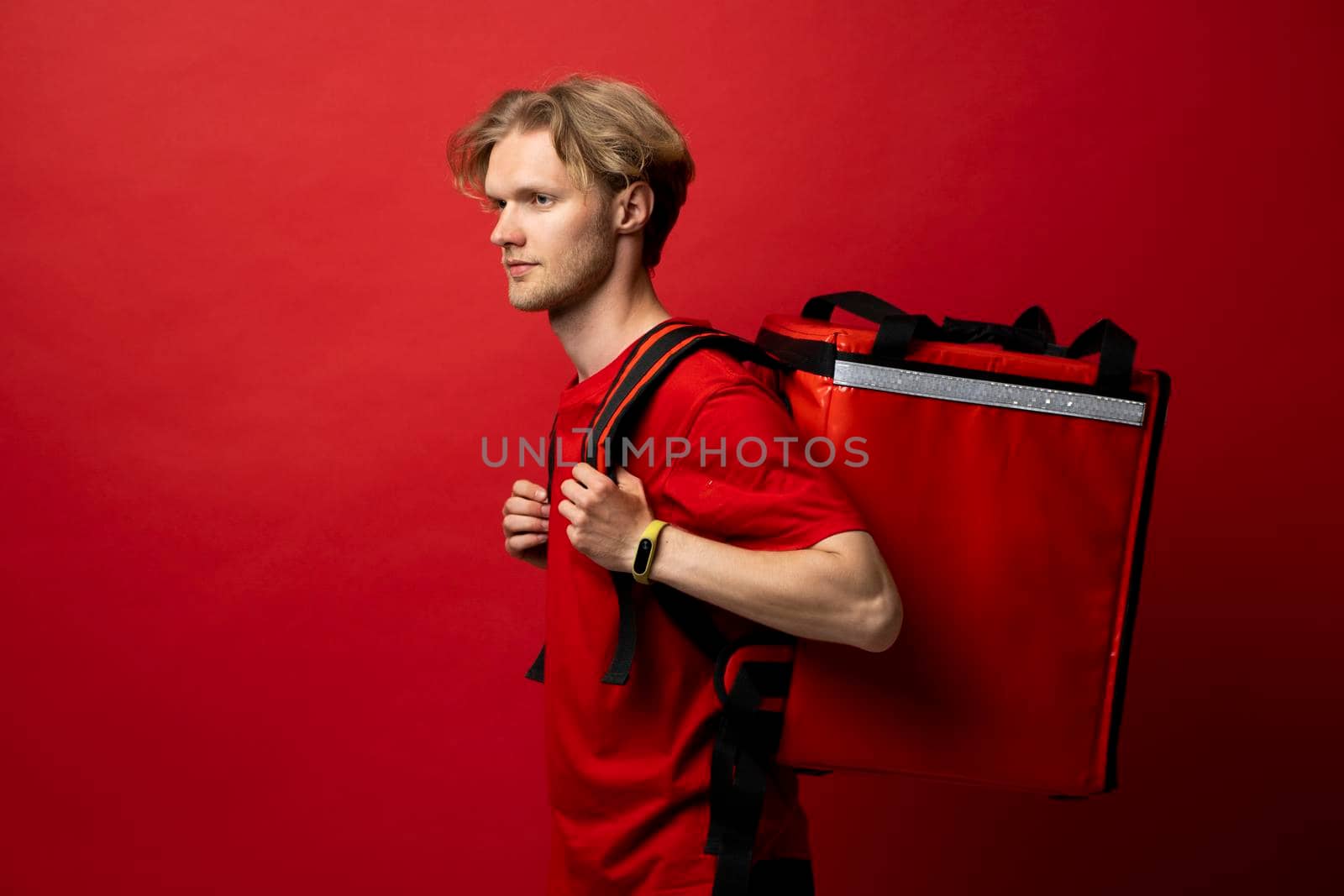 Side view of delivery man in a red t-shirt carry red thermal backpack full of food, groceries to the clients. Food delivery service