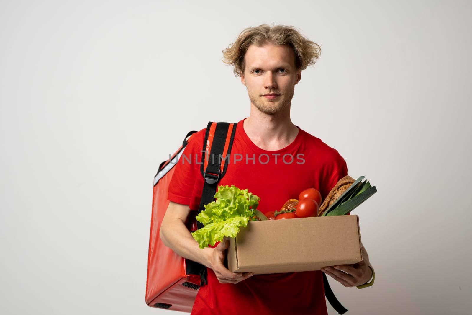 Delivery employee in red t-shirt working courier service from shop restaurant to home holding brown craft paper takeaway food box with vegetables