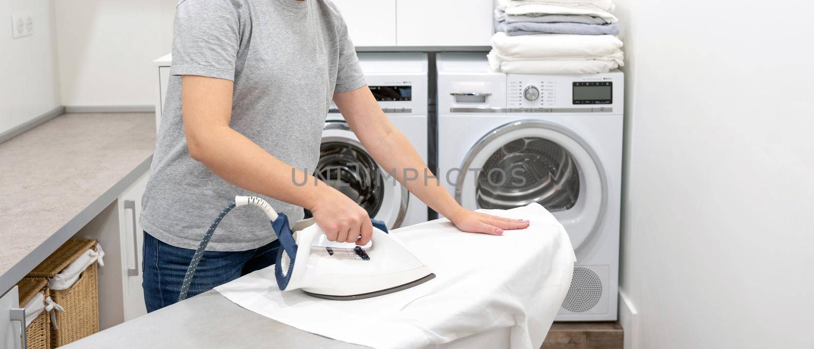 ironing white shirt on board in laundry room with washing machine on background by Mariakray