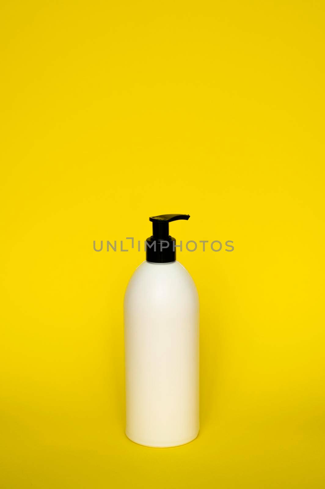 White cosmetic plastic bottle with black pump dispenser on yellow background. Liquid container for gel, lotion, cream, shampoo, bath foam