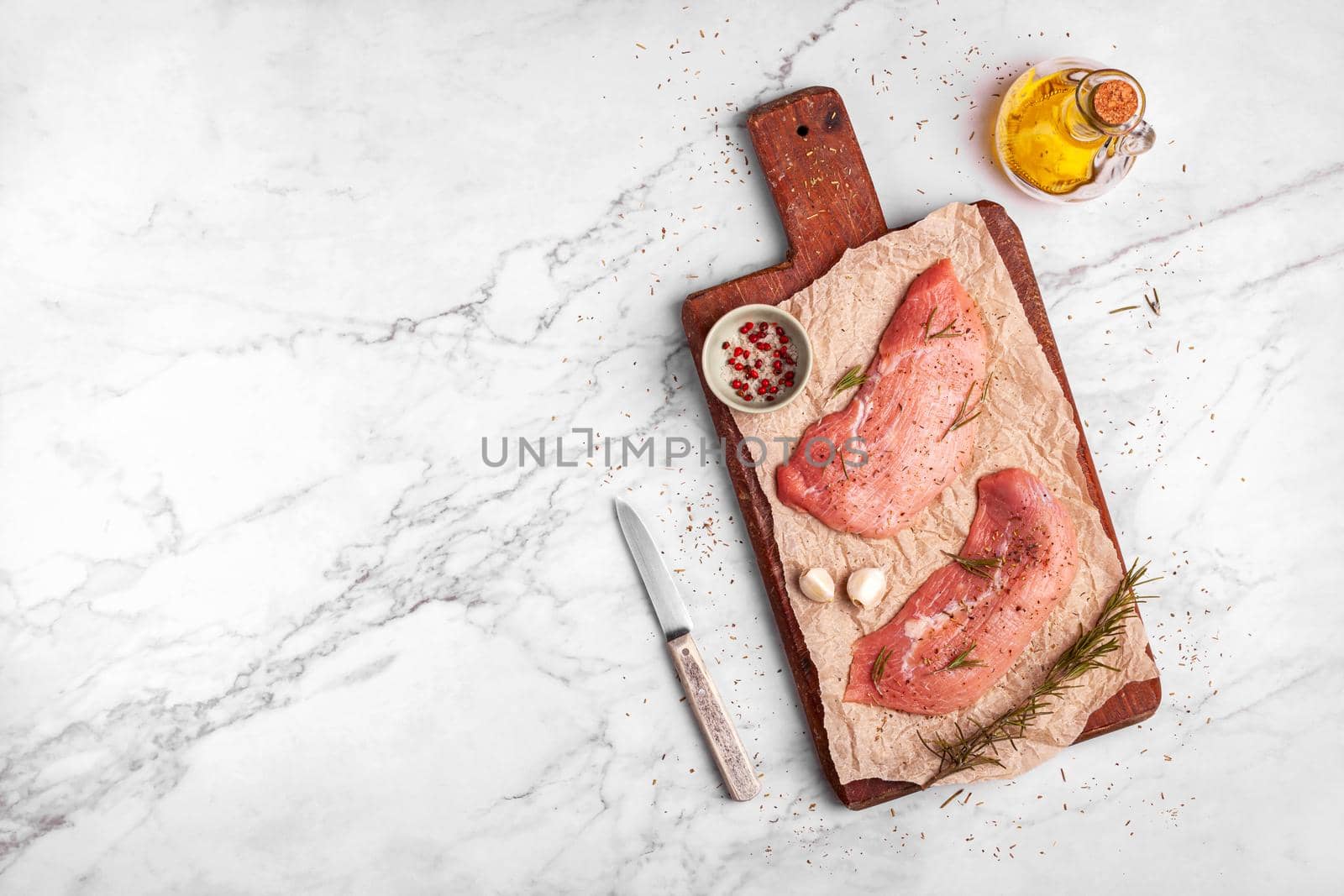 two raw veal escalope on the old wooden cutting board, ready to cook, marbre background, top view, copy space