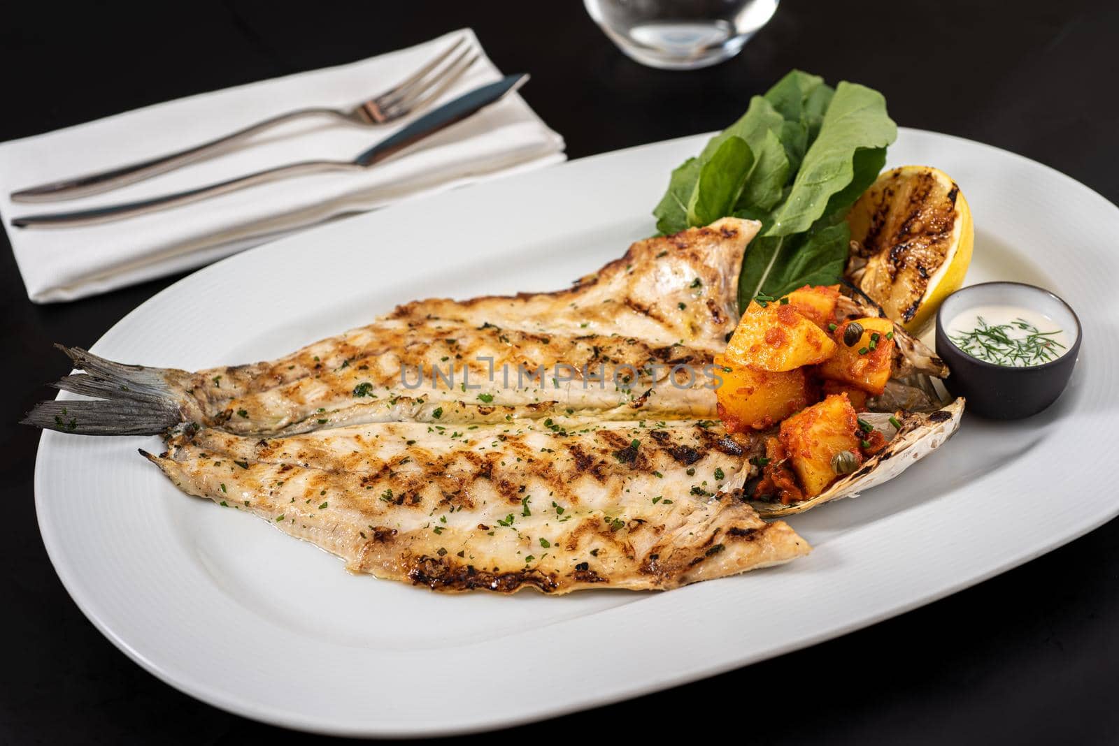 Grilled sea bass and potatoes on a white porcelain plate.