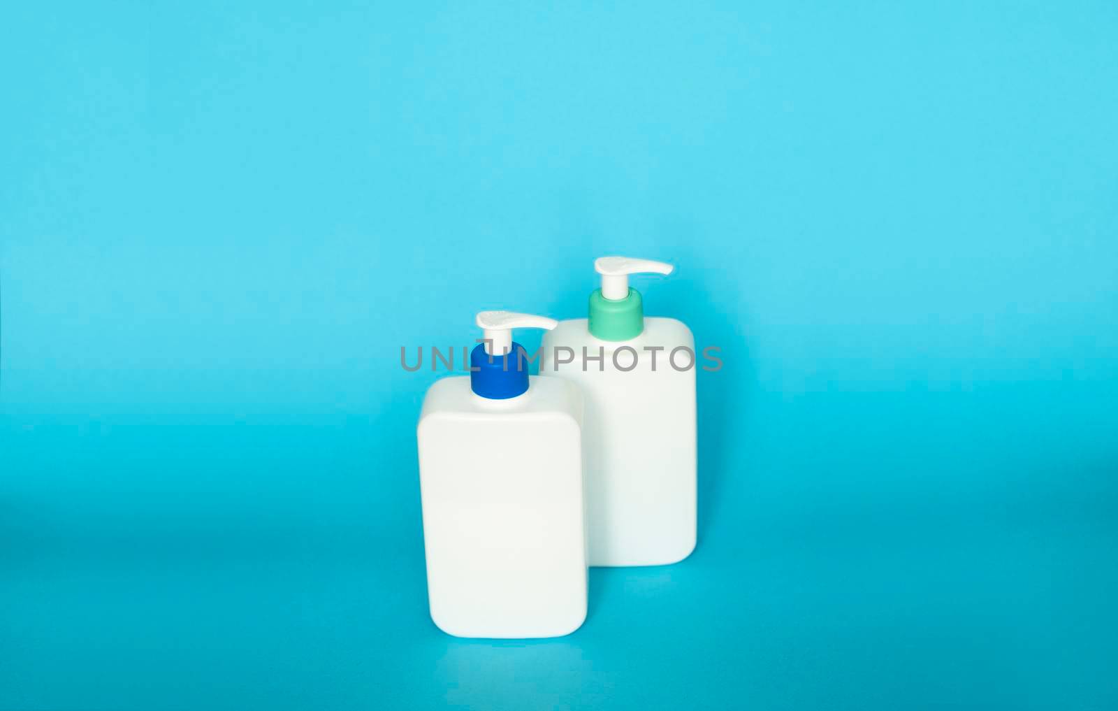 White cosmetic plastic bottles with black pump dispenser on blue background. Liquid containers for gel, lotion, cream, shampoo, bath foam