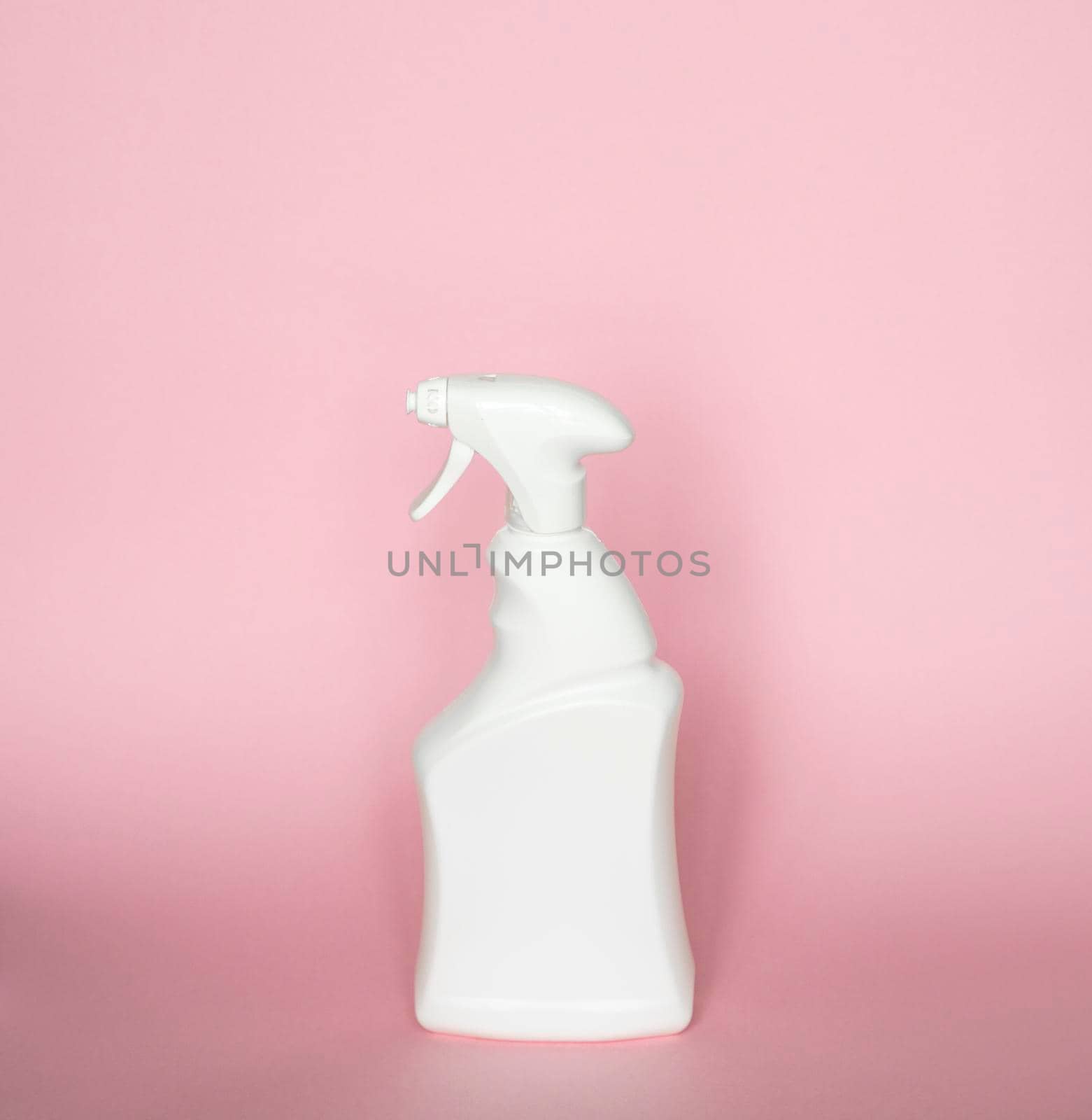 White detergent bottles or chemical cleaning supplies with a sprayer isolated on pink background